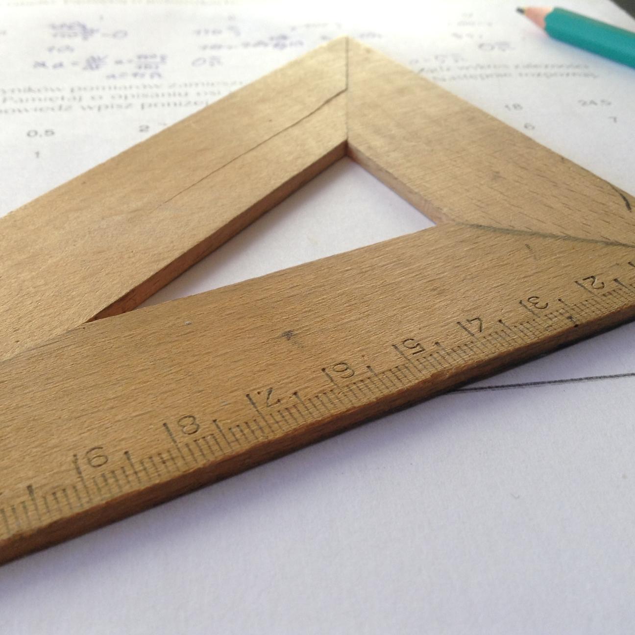 Ein Geodreieck aus Holz liegt auf einem beschriebenen Blatt, daneben ein grüner Bleistift.