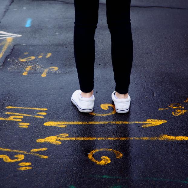 Eine Person steht auf einer Straße, die mit mehreren kryptischen Zeichen und Pfeilen bemalt ist