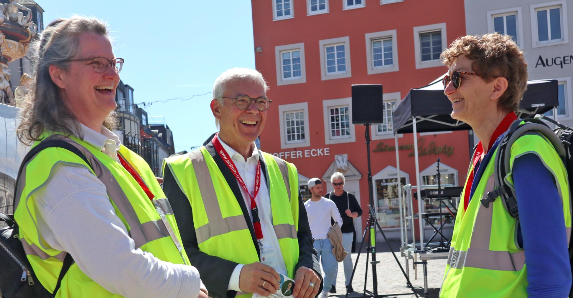 Zwei Frauen und ein Mann mit Warnwesten stehen auf dem Hauptmarkt und lachen sich an