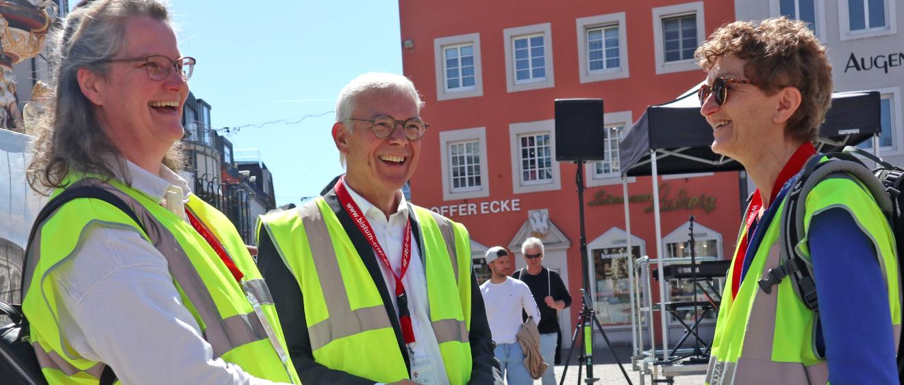 Zwei Frauen und ein Mann mit Warnwesten stehen auf dem Hauptmarkt und lachen sich an