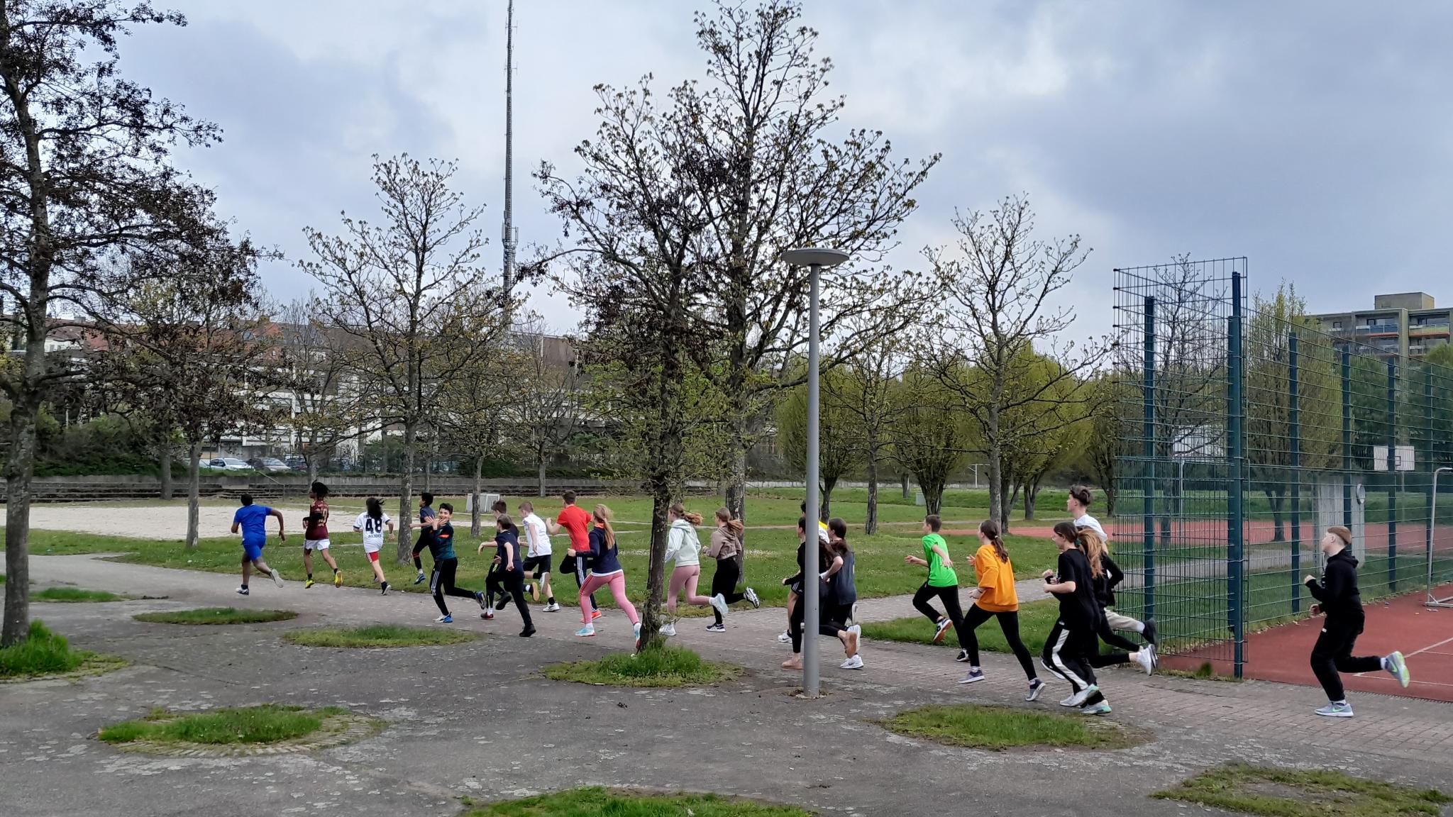 Kinder in Sportkleidung beim Joggen, vorbei an einem Sportgelände