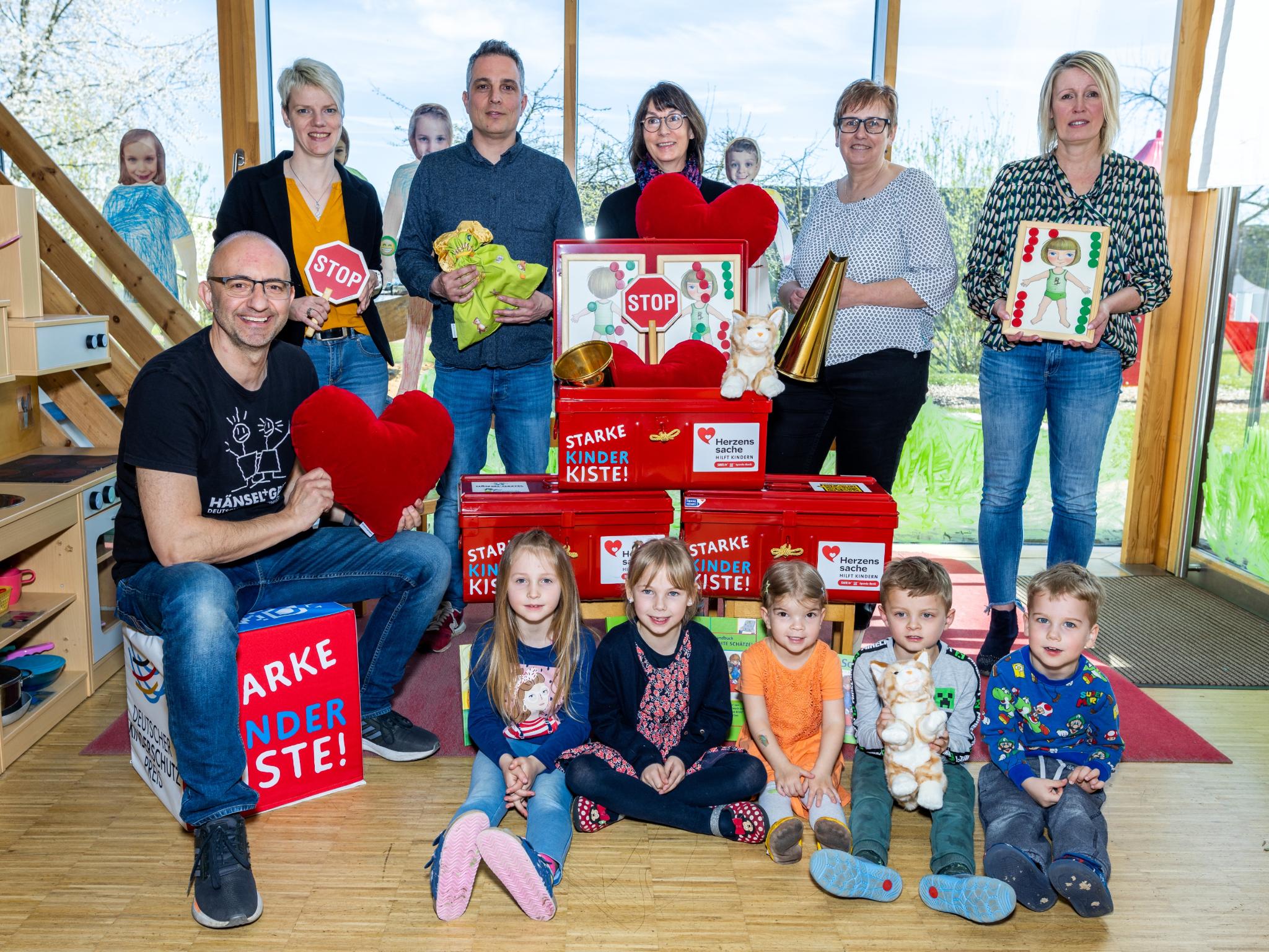 Kinder und Erwachsene mit Mini-STOP-Schildern, Spielsachen und einer Puppenküche