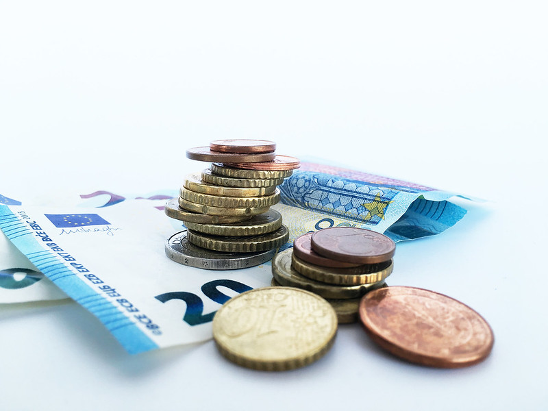 Das Foto zeigt in Großaufnahme vor weißem Hintergrund einen 20-Euro-Schein und darauf und daneben gestapelt Euro- und Cent-Münzen.