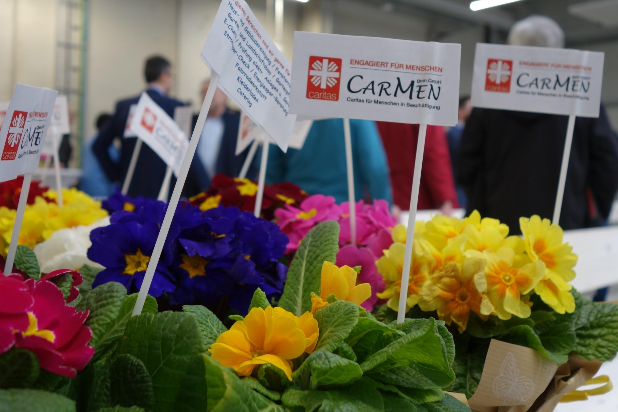 Blumen stehen auf einem Tisch, darin Zettel auf denen CarMen gGmbH steht.