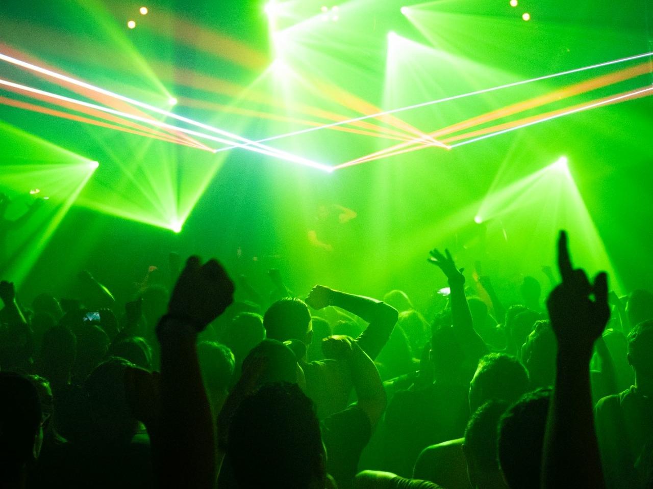 Tnanzende Menge im Club bei grünem Licht; im Hintergrund ein D.J.