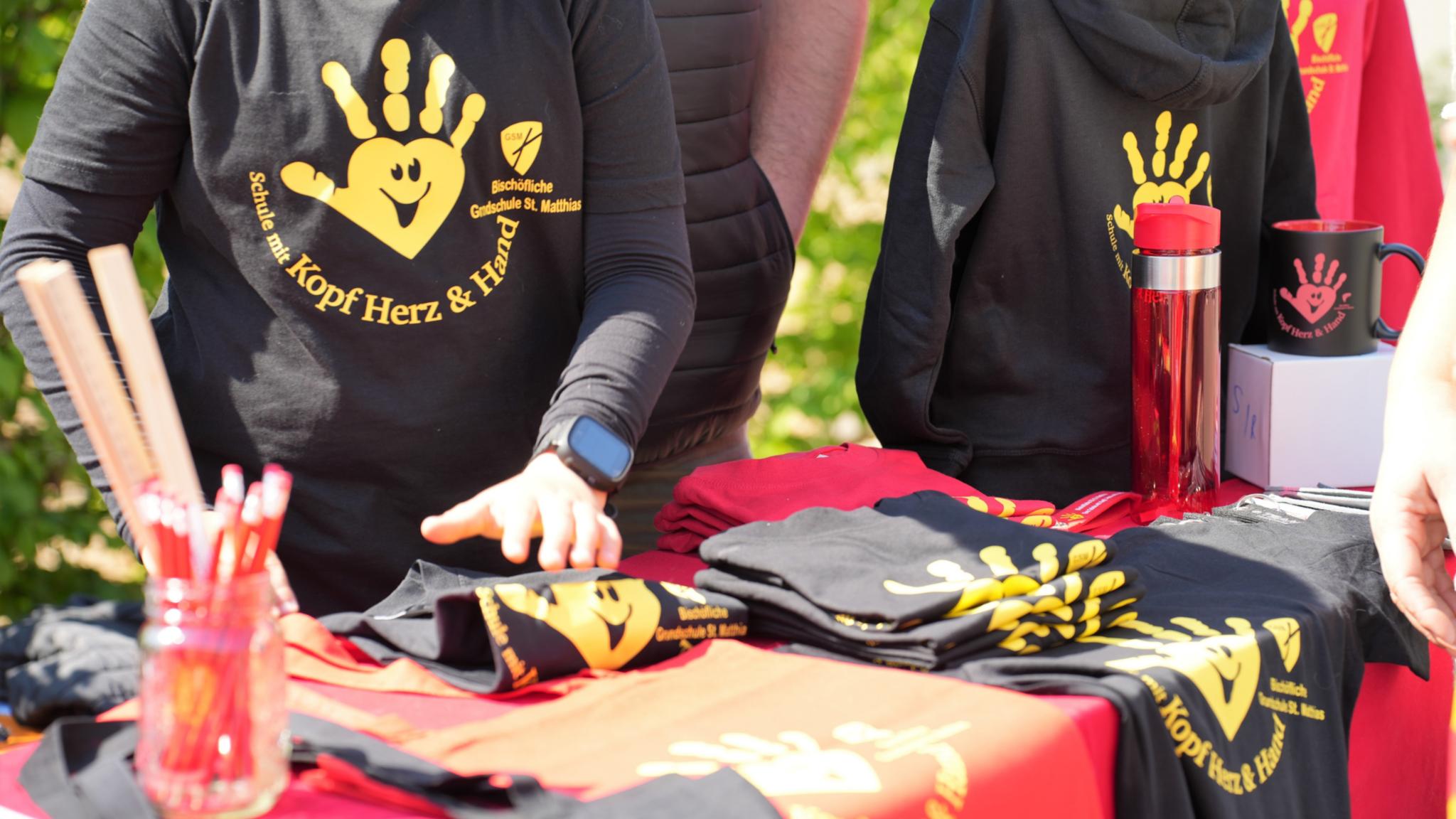 „Schule mit Kopf, Herz und Hand“: Ein Stand verkauft beim Schulfest Shirts und Utensilien mit dem Schulmotto.