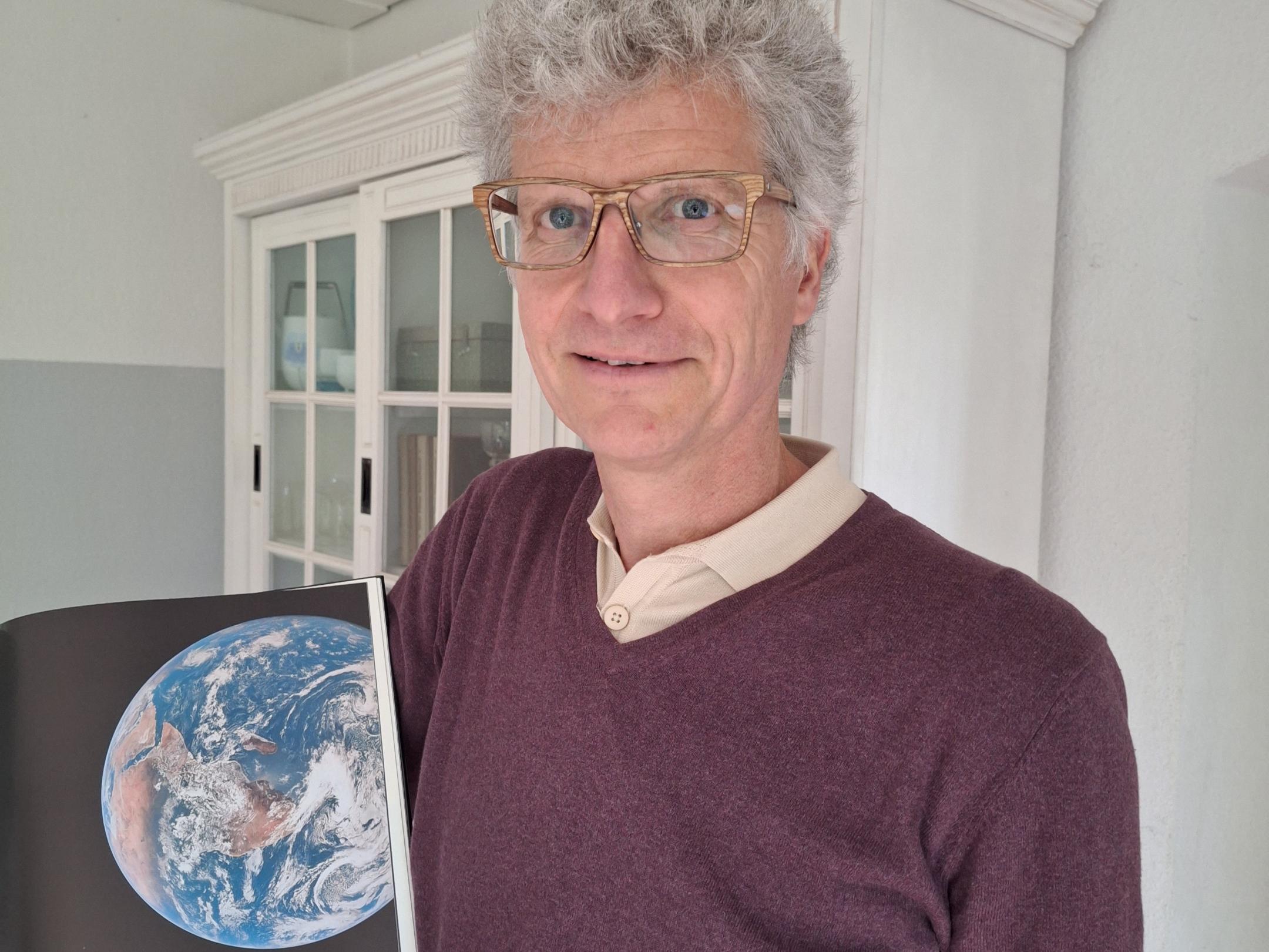 Ein Foto von Manuel Frey, wie er ein Buch zeigt, in dem die Welt abgebildet ist