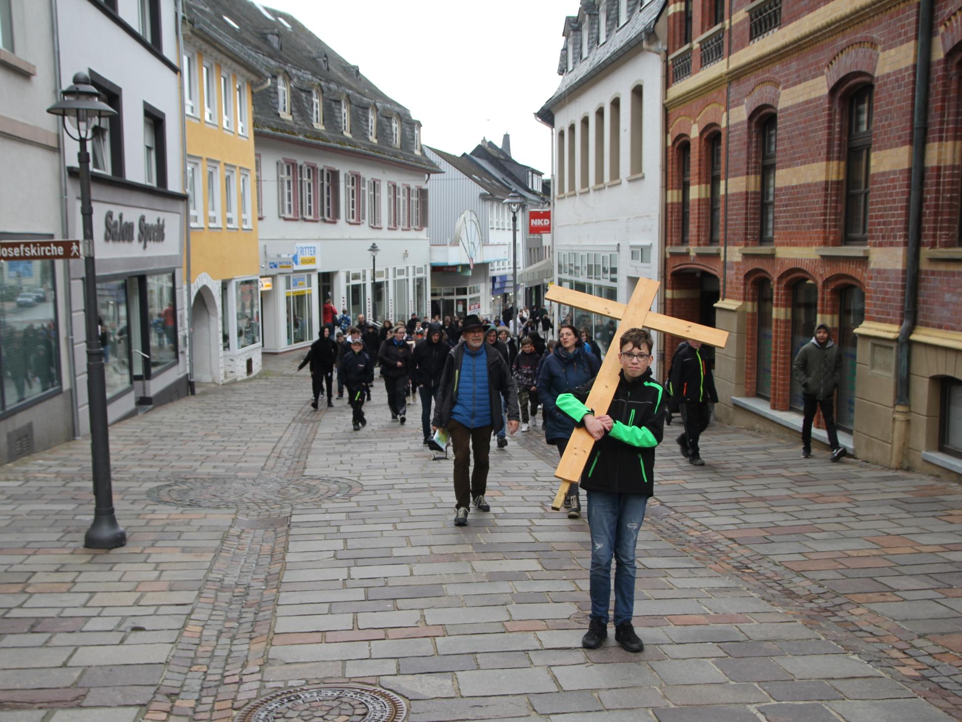 Ein Junge mit einem großen Kreuz zieht durch eine Fußgängerzone.