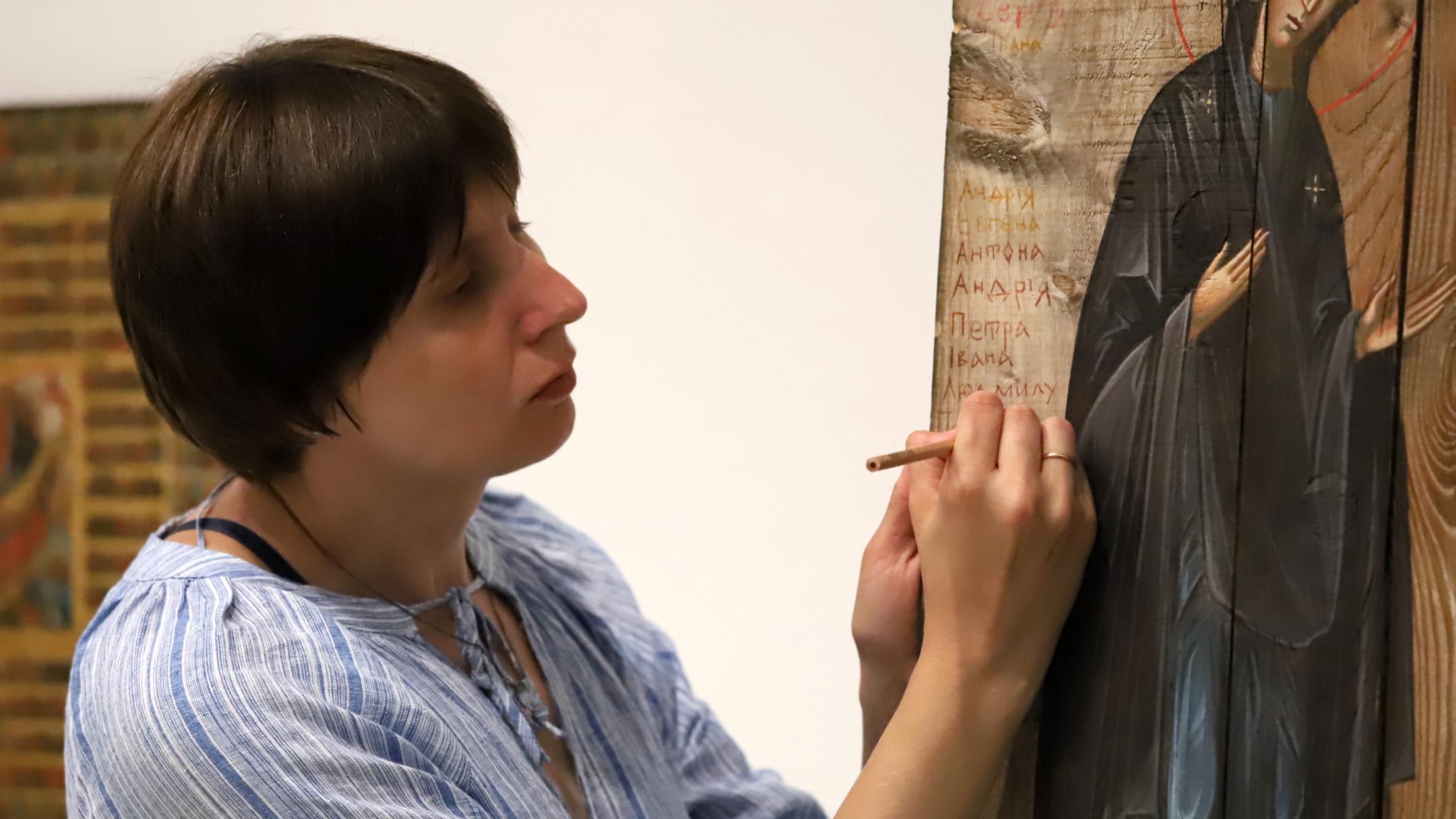 Sofia Atlantova schreibt mit einem dünnen Buntmalstift den ersten Namen eines ukrainischen Kriegsopfers auf das raue Holz