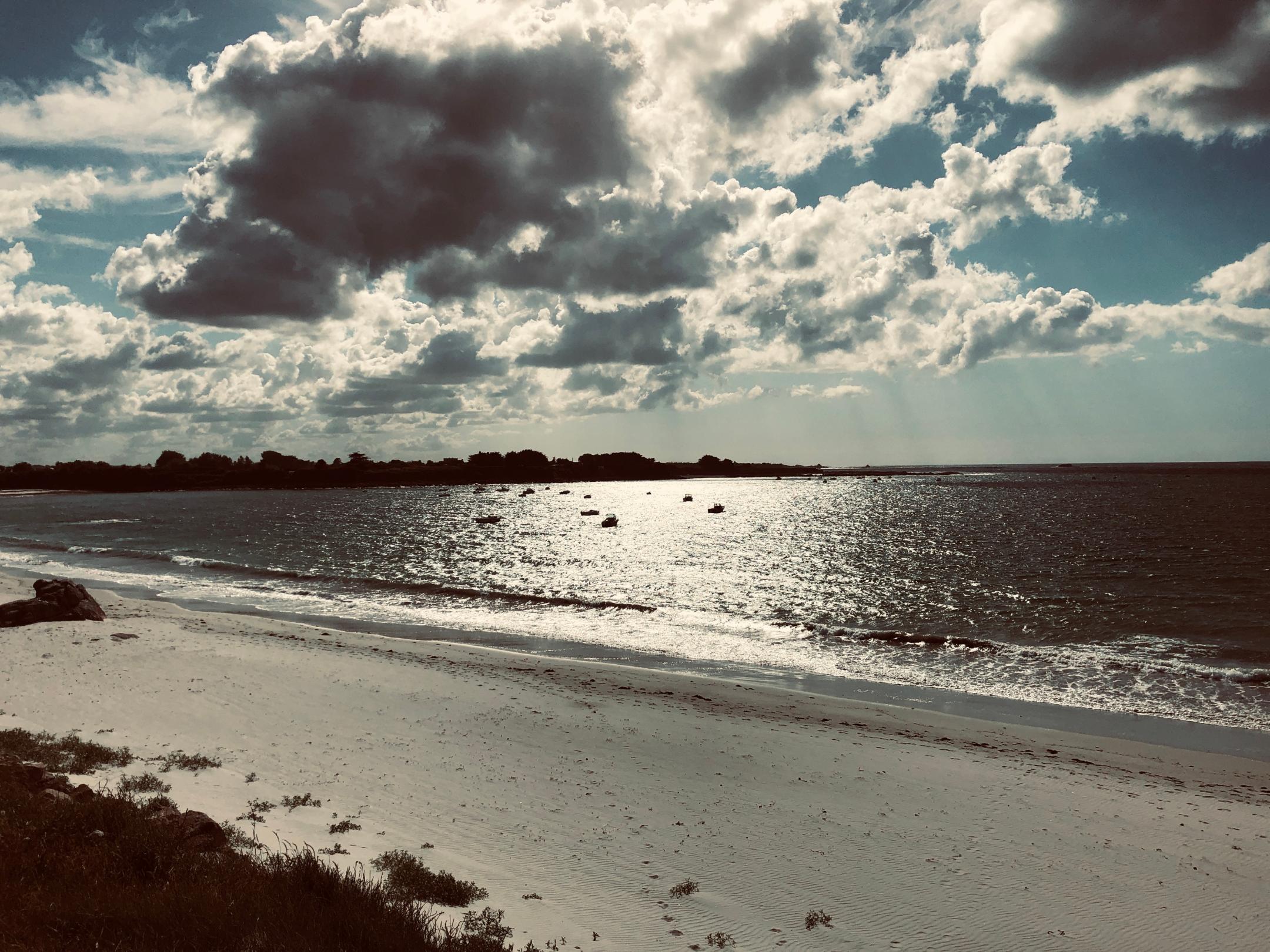 Die Sonne scheint auf einen Strand am Meer mit kleinen Booten auf dem Wasser.