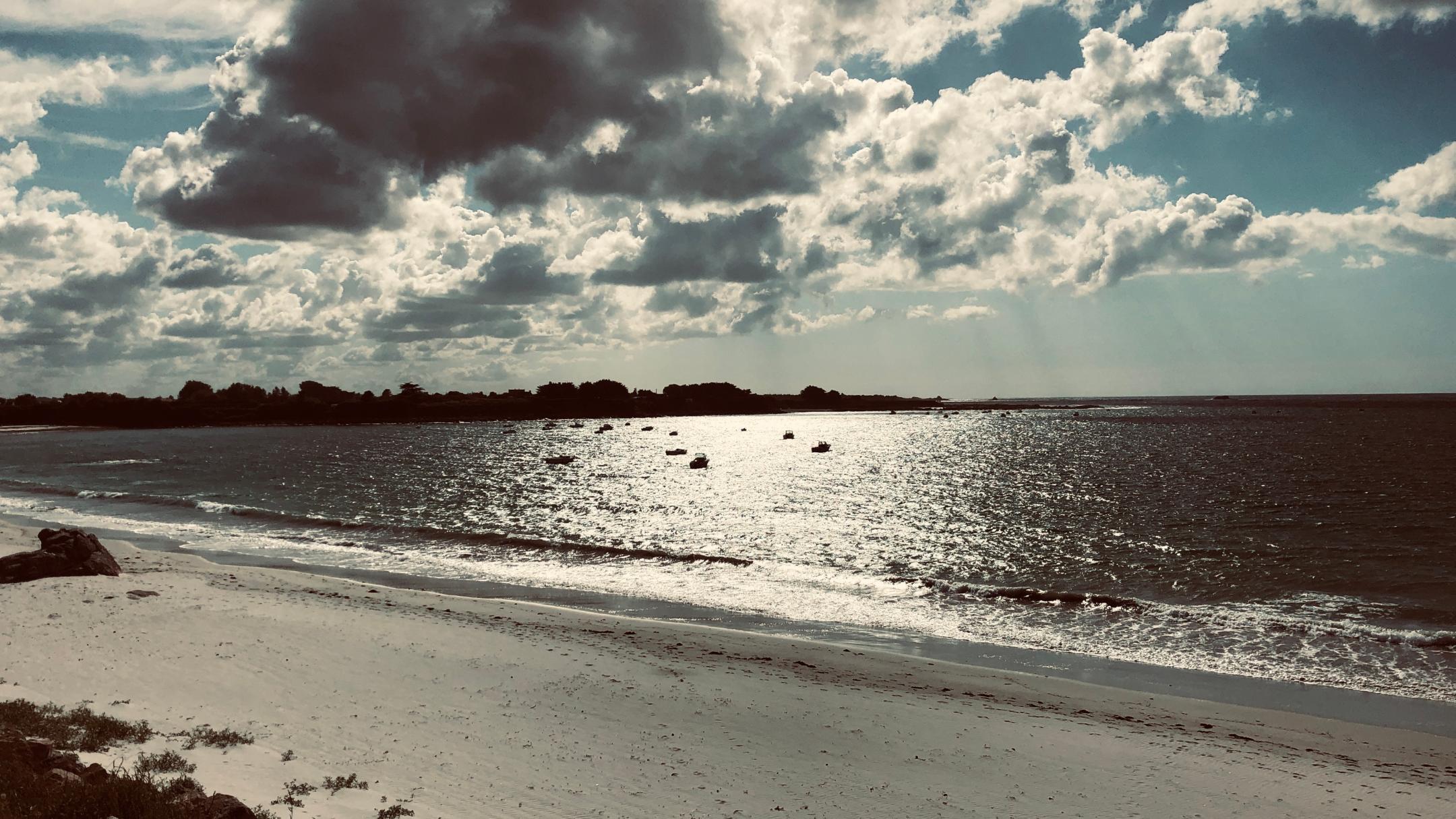 Die Sonne scheint auf einen Strand am Meer mit kleinen Booten auf dem Wasser.