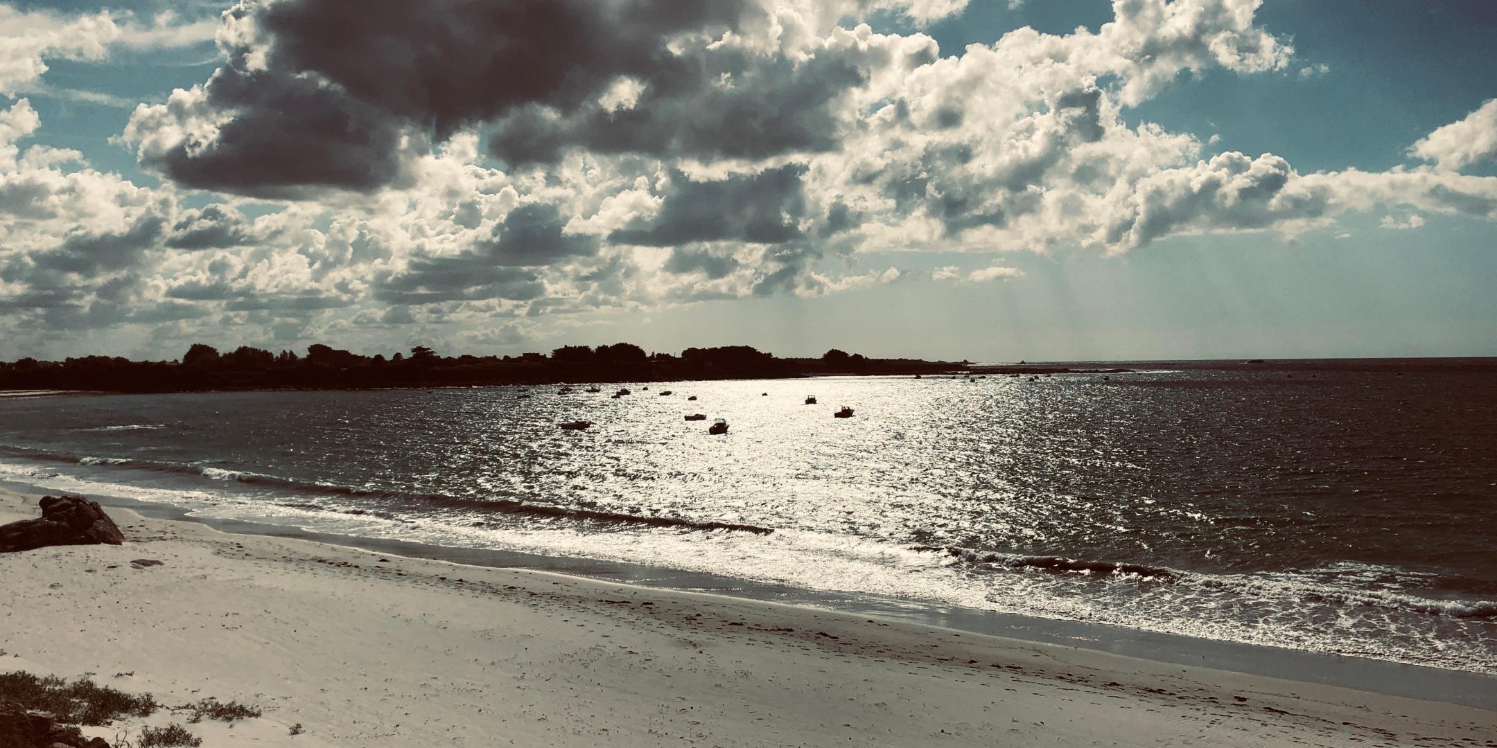Die Sonne scheint auf einen Strand am Meer mit kleinen Booten auf dem Wasser.