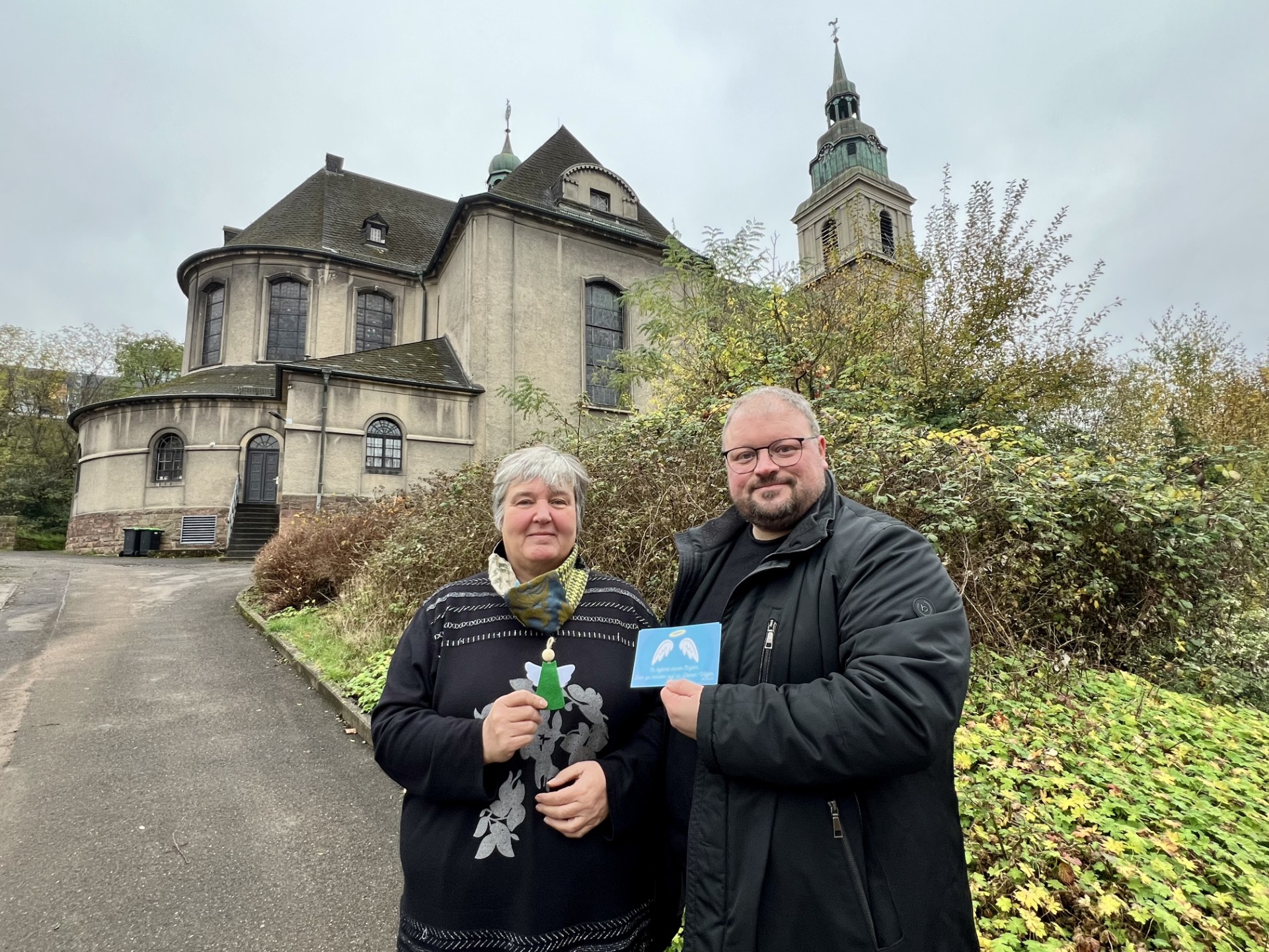 Zwei Menschen stehen vor einer Kirche und präsentieren eine Karte, die sie in der Hand halten