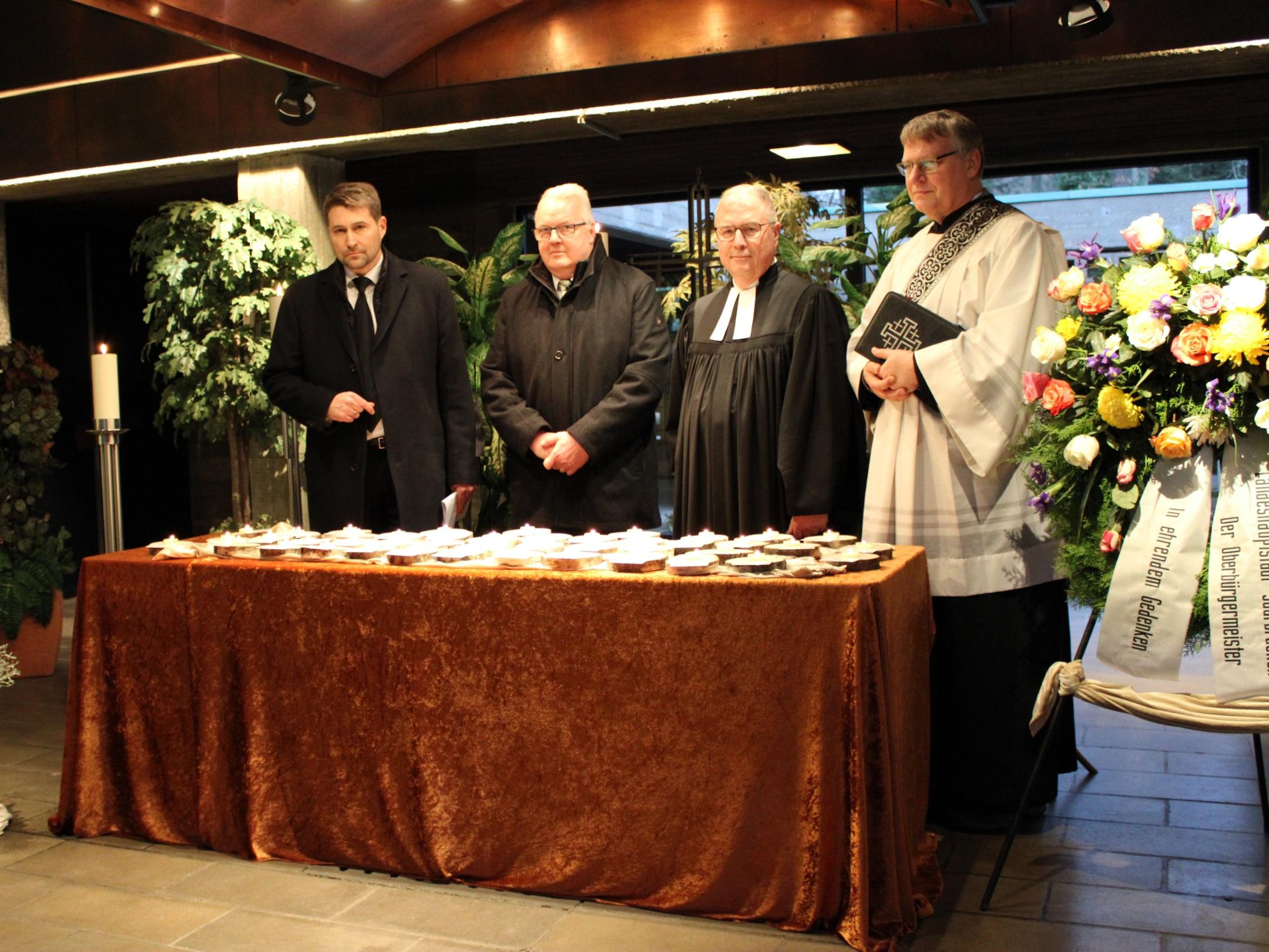 Oberbürgermeister Uwe Conradt, Christian Duchene (Bestatterverband), Superintendent Christian Weyer und Diakon Gerd Fehrenbach vor den Gedenkkerzen für die 40 einsam Verstorbenen im vergangenen Jahr Foto: evks/Rieke Eulenstein