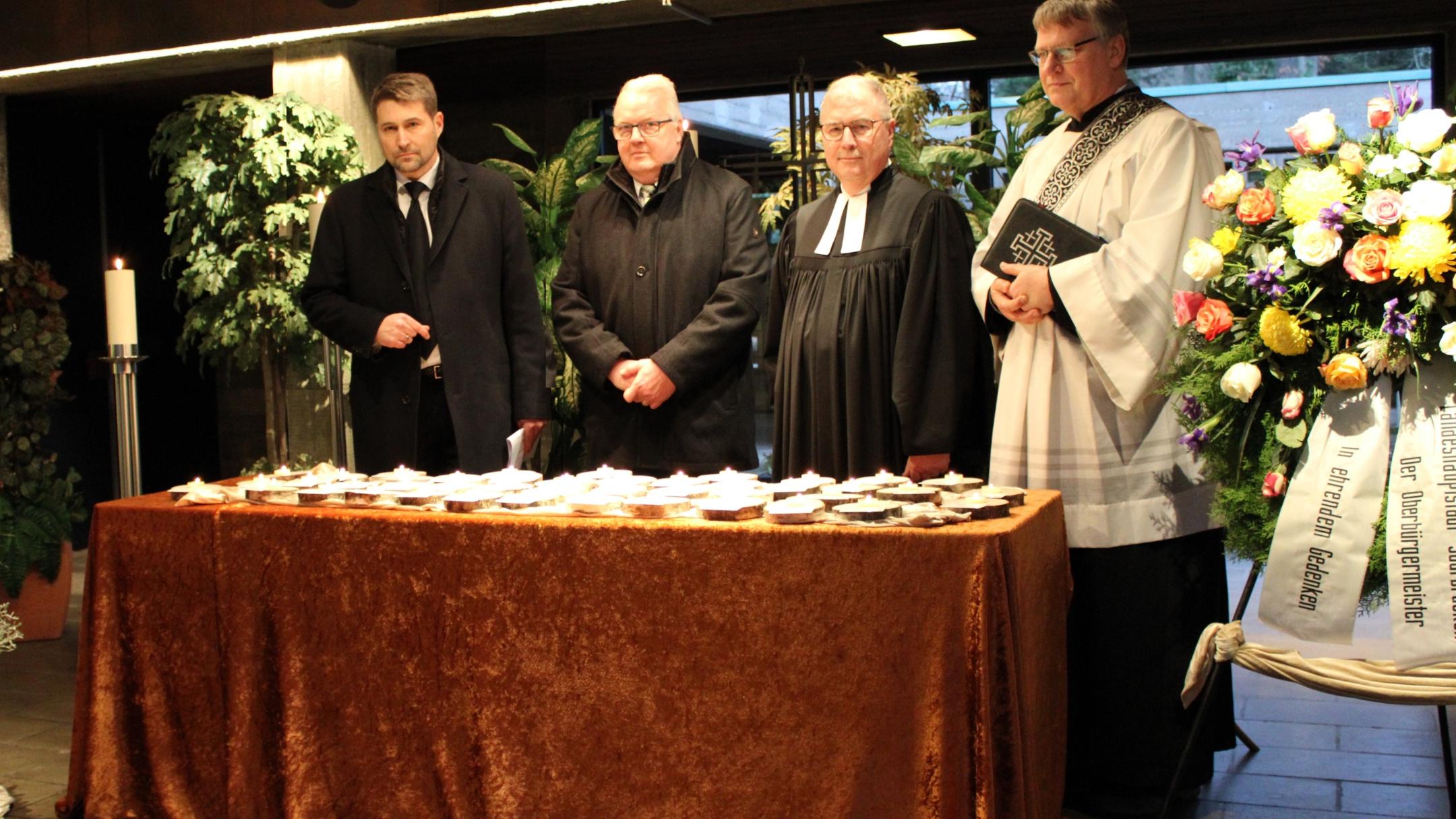 Oberbürgermeister Uwe Conradt, Christian Duchene (Bestatterverband), Superintendent Christian Weyer und Diakon Gerd Fehrenbach vor den Gedenkkerzen für die 40 einsam Verstorbenen im vergangenen Jahr Foto: evks/Rieke Eulenstein