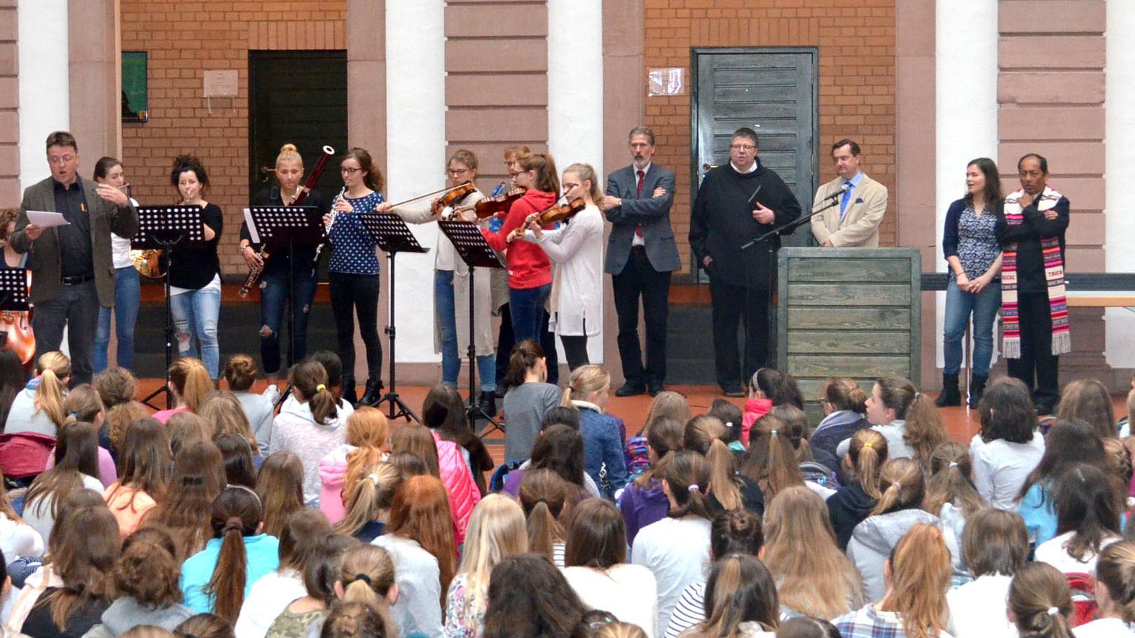 Im Hintergrund neben dem Orchester des AMG stehen von links nach rechts Ludwig Kuhn von der Diözesanstelle Weltkirche, Schulseelsorger Bruder Gregor, Direktor Dr. Mario Zeck und Erzbischof Ricardo Centellas.