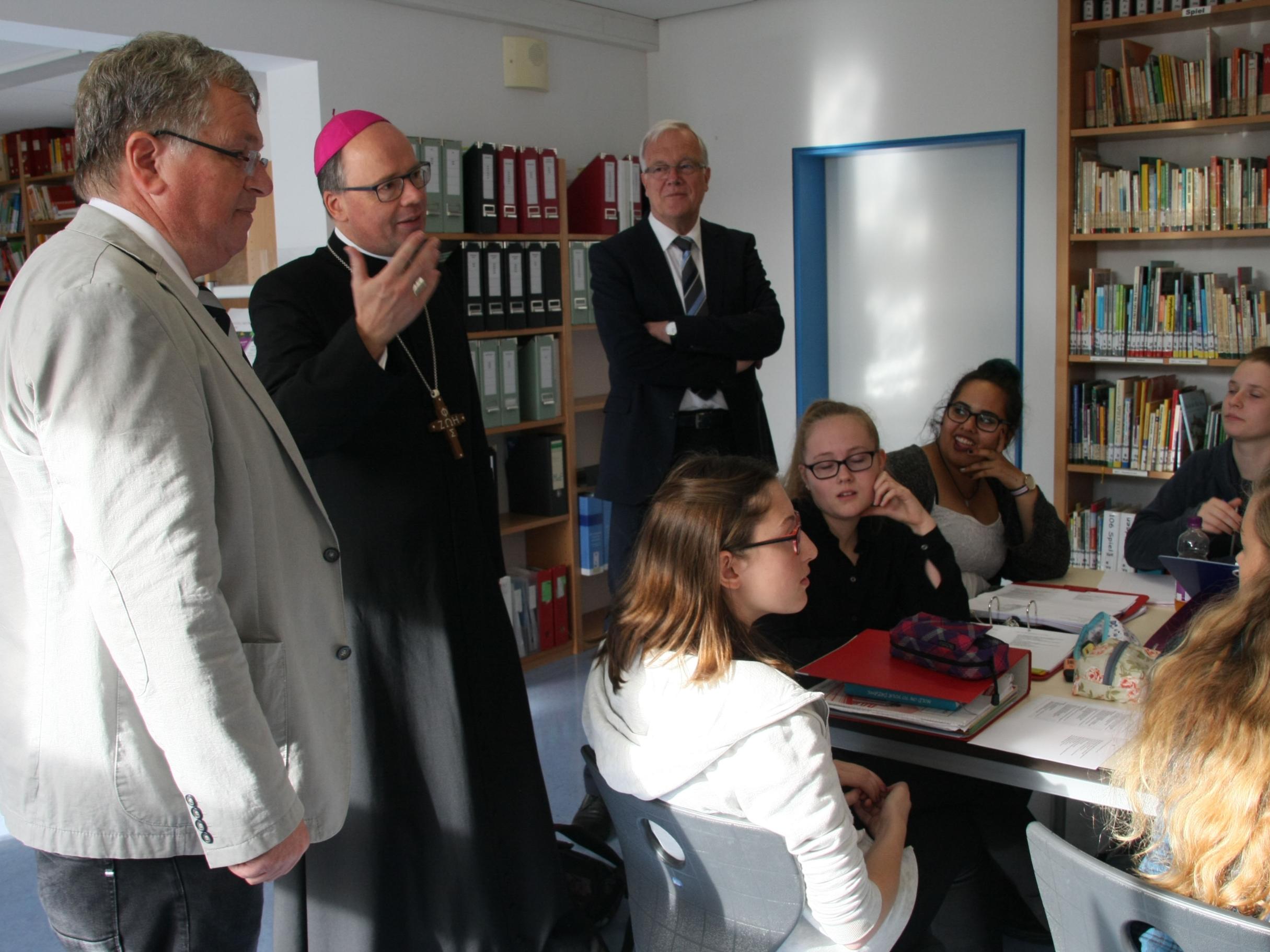 In der Bibliothek treffen Bischof Dr. Stephan Ackermann (Mitte), Wolfgang Müller vom Bischöflichen Generalvikariat (rechts) und Schulleiter Thomas Schmitz auf eine Gruppe von Schülerinnen, die sich auf ein anstehendes Referat vorbereiten.