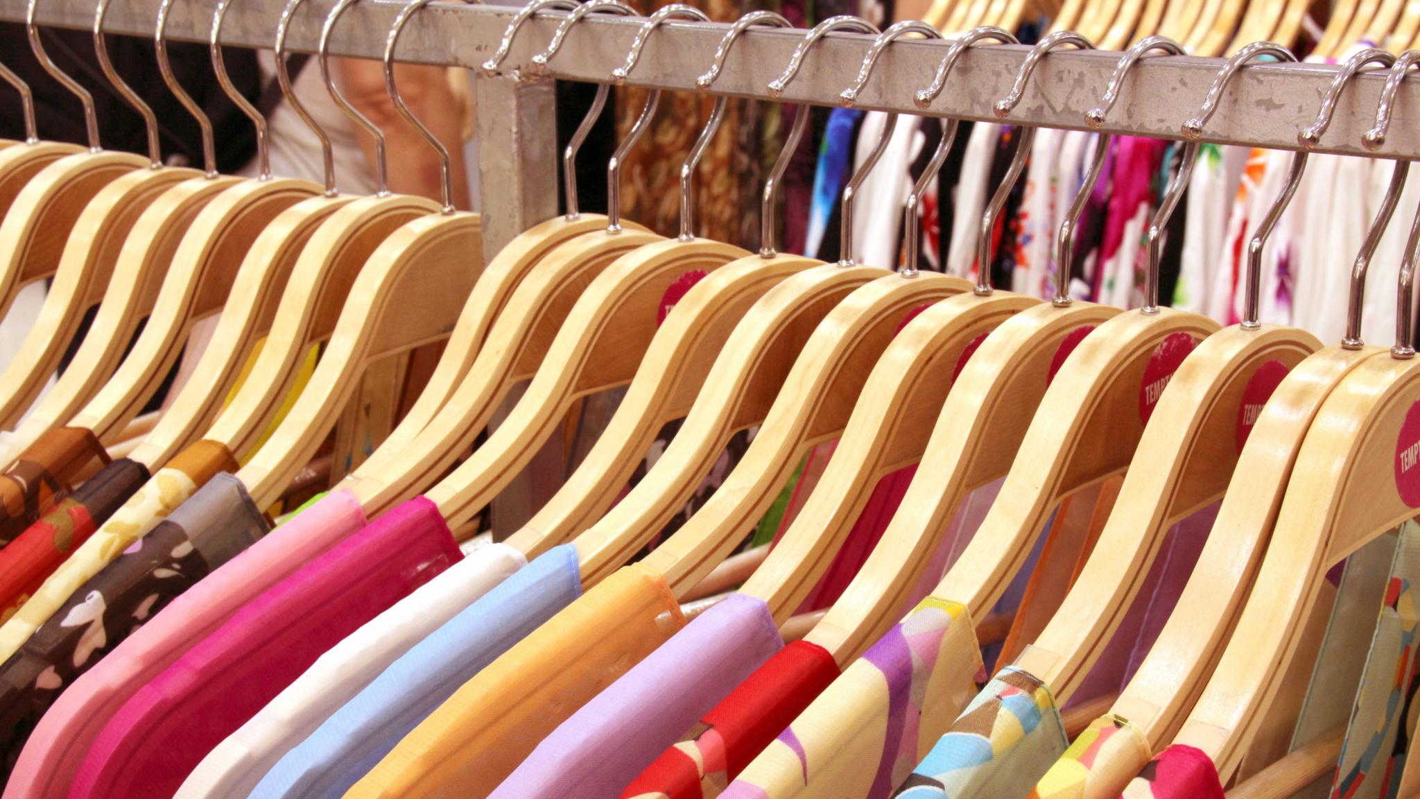 Kleider auf Holzkleiderbügeln an einer Kleiderstange, verschiedene Farben und Muster.