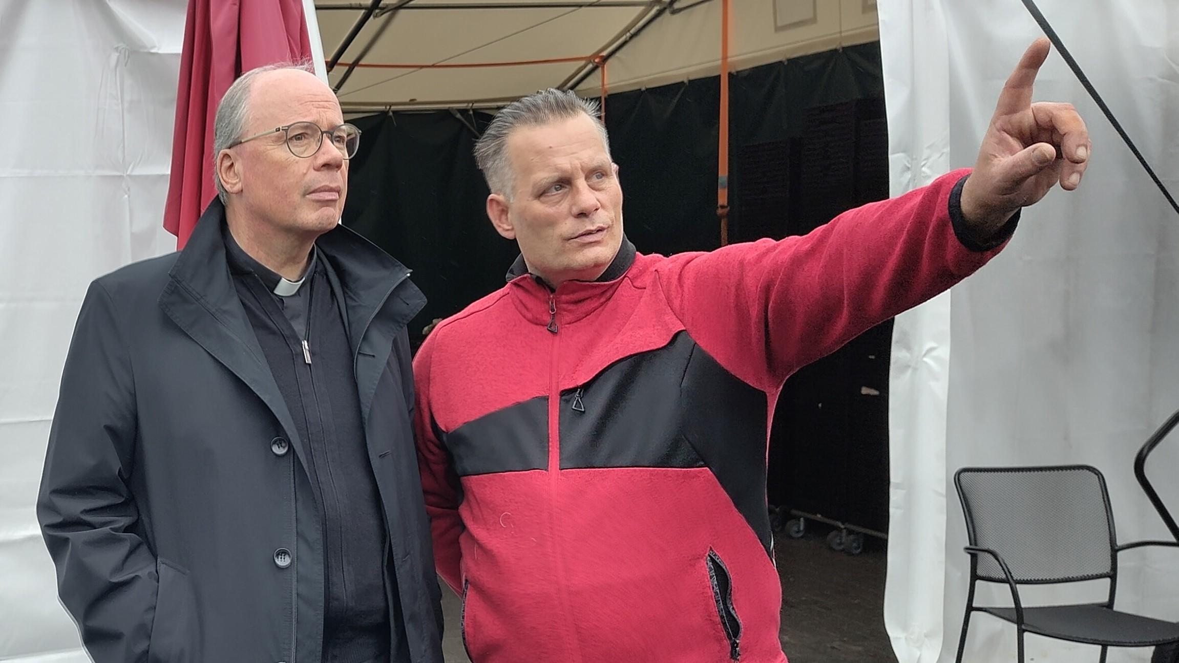 Markus Oehlschläger in roter Trainingsjacke weist Bischof Ackermann mit dem Zeigefinger auf etwas hin, das außerhalb des Bildes liegt.