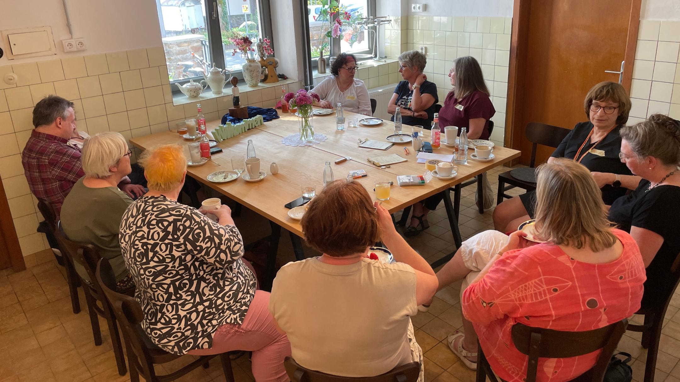 10 Frauen und ein Mann sitzen um einen gedeckten Tisch.