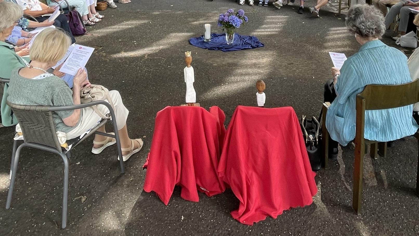 Die Königsfiguren stehen jede für sich auf einem mit einem roten Tuch verkleideten Hocker, im Kreis der Teilnehmerinnen.