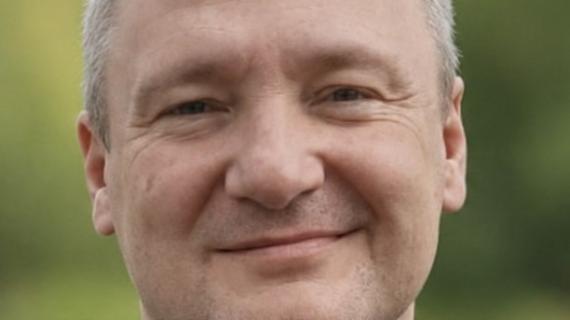 Pfarrer Konrad Lisowski, ein Mann mit leicht ergrauten, kurzen Haaren, die sich im Stirnbereich lichten, blickt verschmitzt in die Kamera.