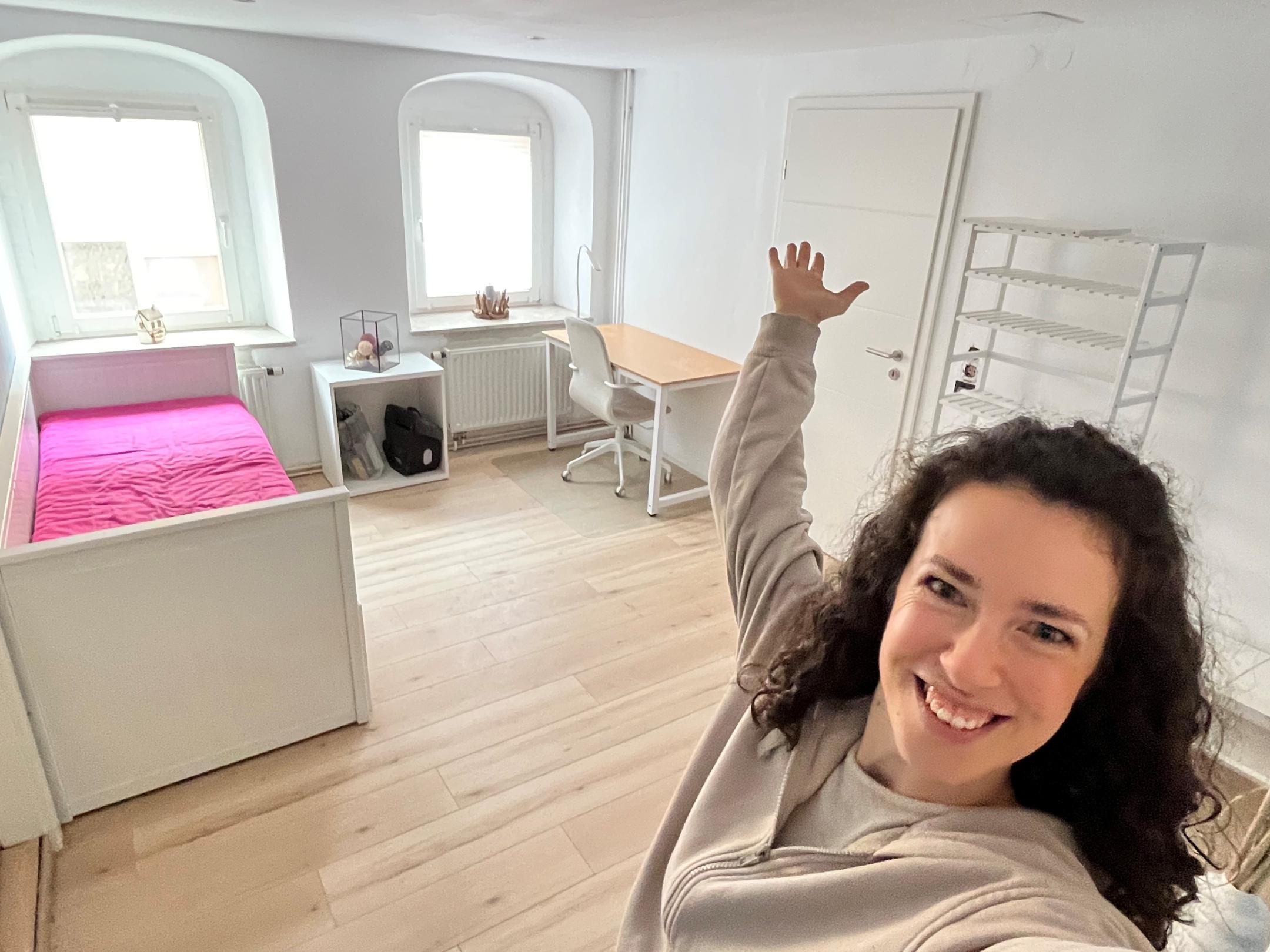 Eine junge Frau streckt die Hand aus und zeigt in ein Zimmer