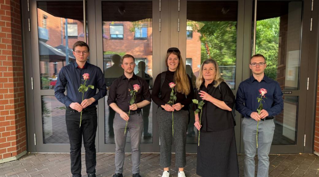 Dunkel gekleidete Menschen blicken in die Kamera und halten Rosen in den Händen