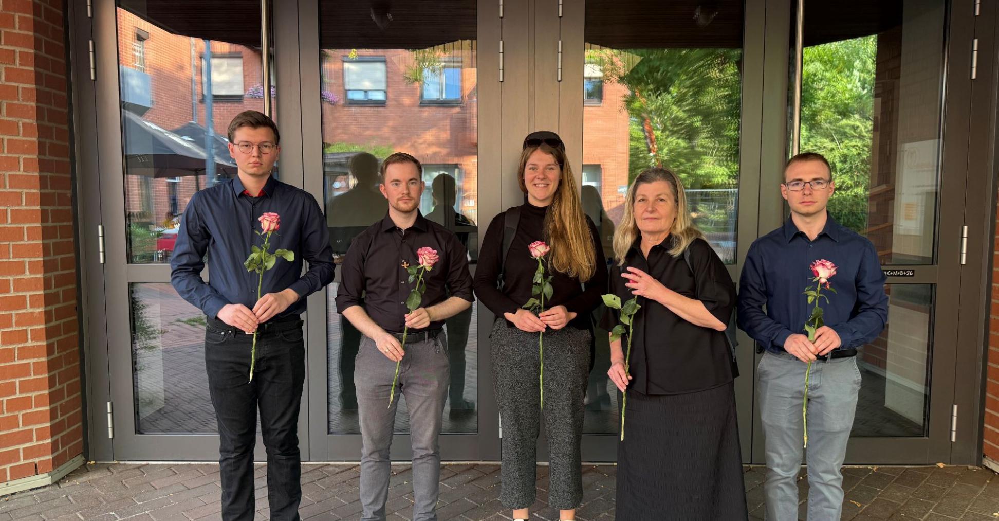 Dunkel gekleidete Menschen blicken in die Kamera und halten Rosen in den Händen