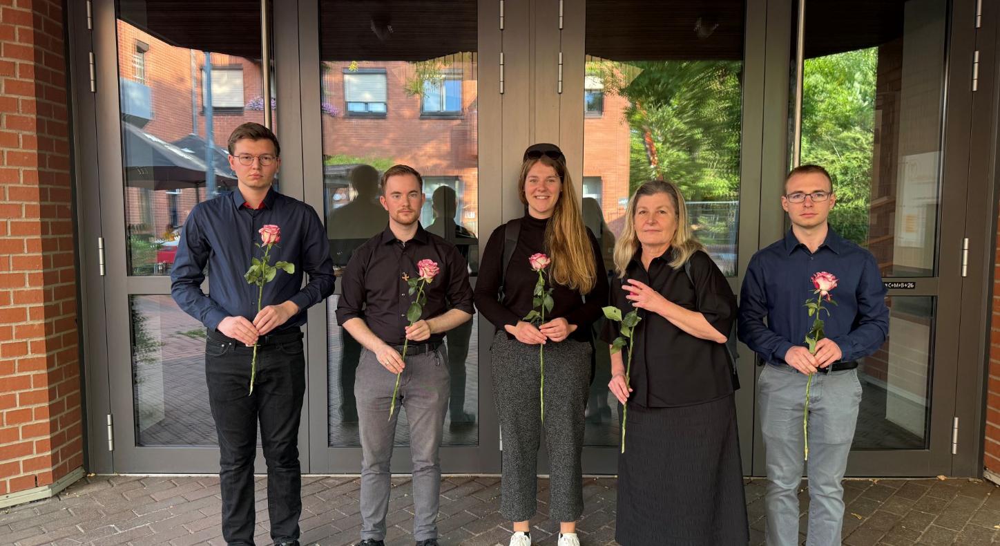 Dunkel gekleidete Menschen blicken in die Kamera und halten Rosen in den Händen