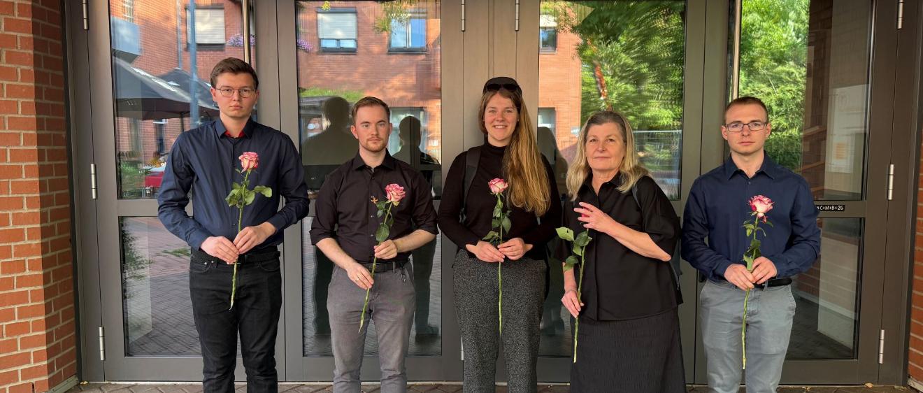 Dunkel gekleidete Menschen blicken in die Kamera und halten Rosen in den Händen