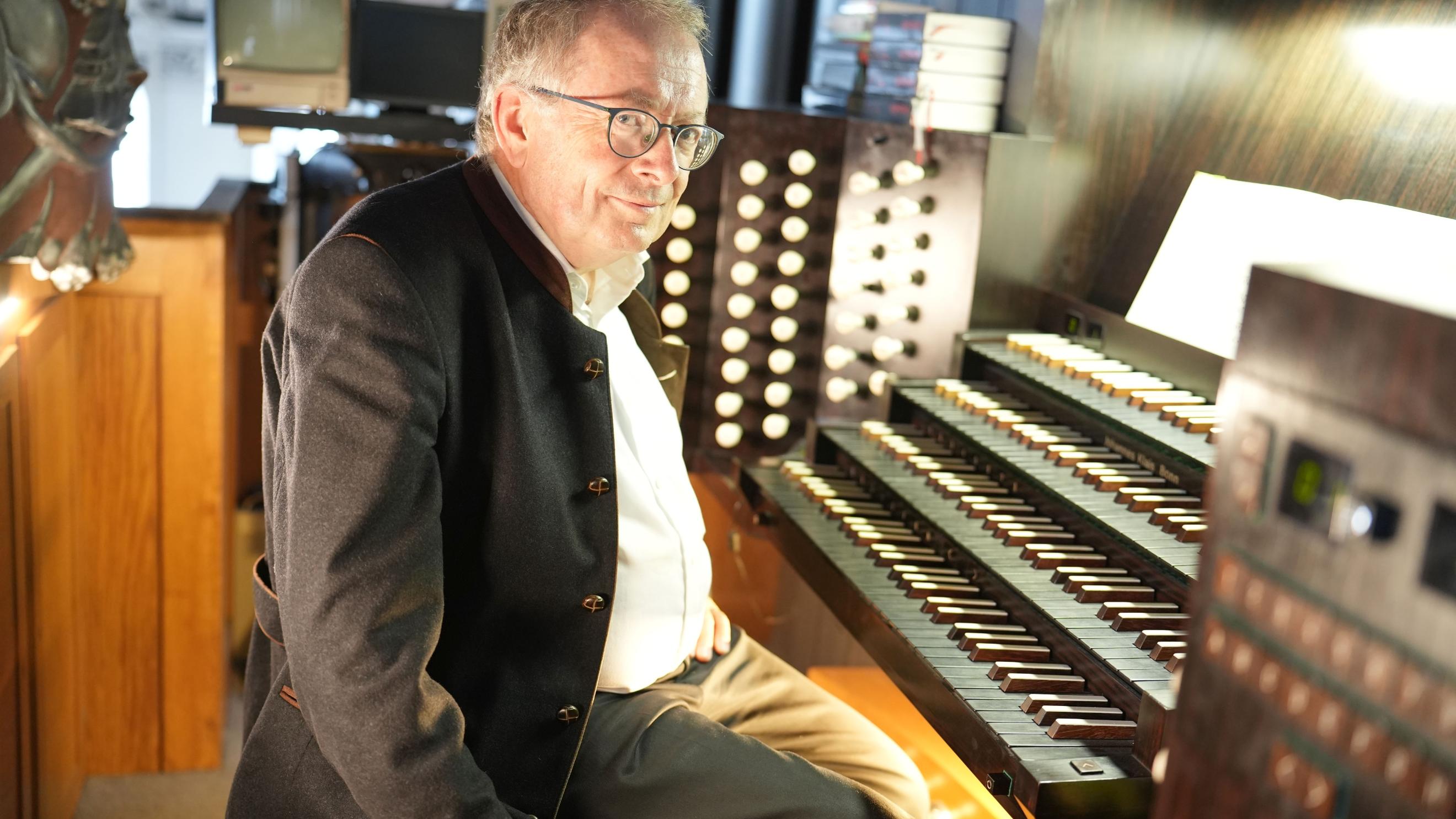 Ein Mann sitzt an einer Orgel und blickt in die Kamera