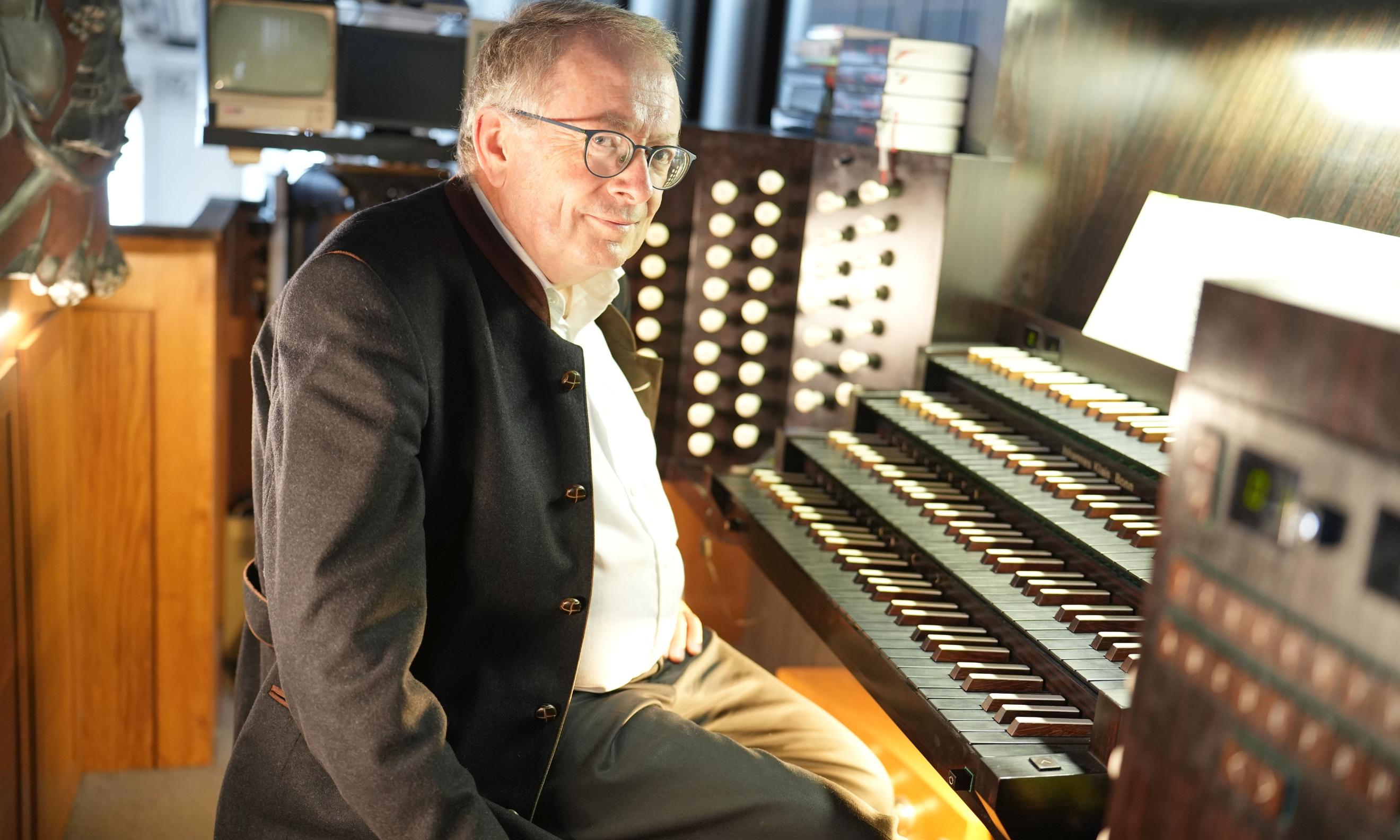 Ein Mann sitzt an einer Orgel und blickt in die Kamera