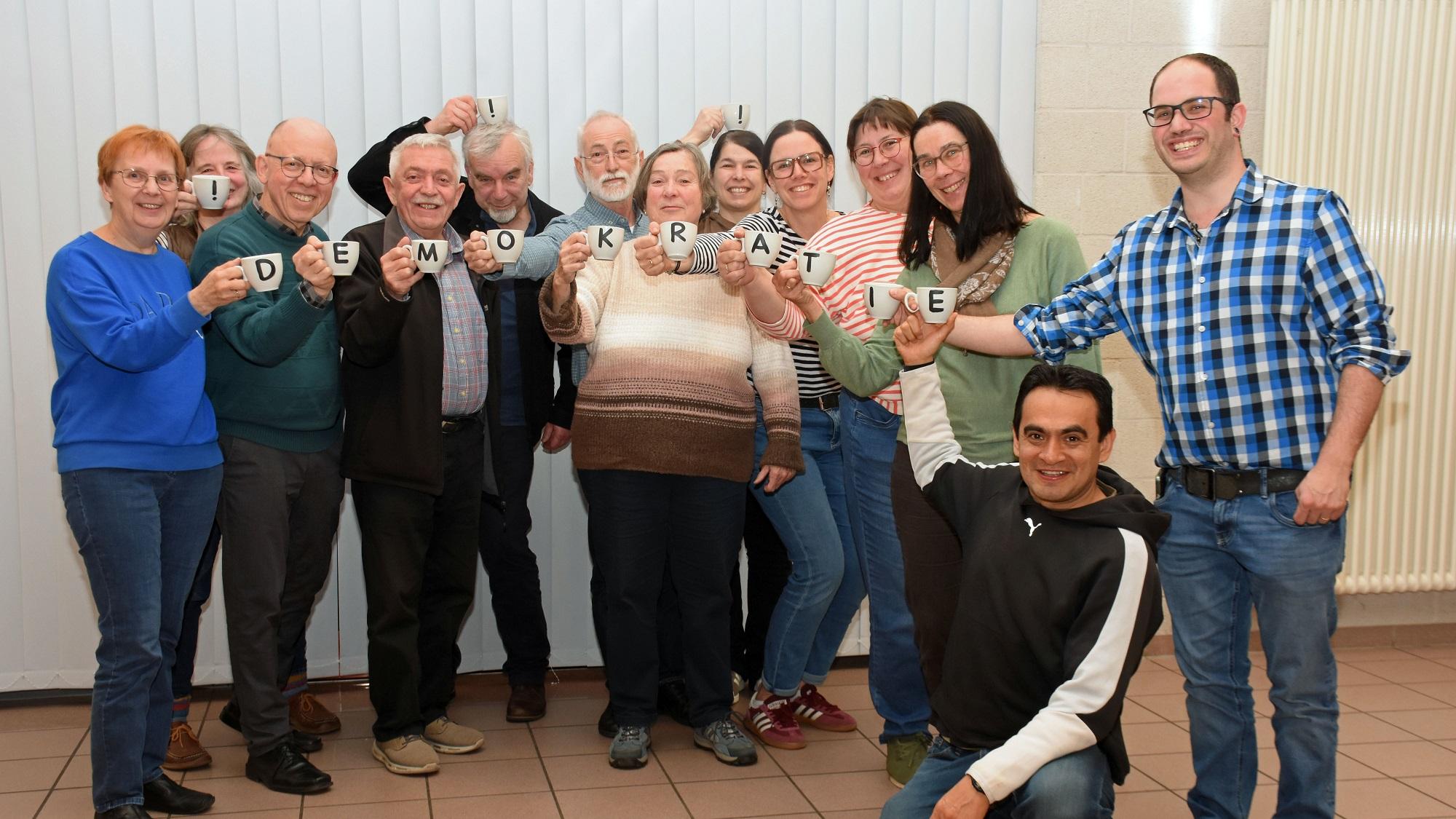 Die Mitglieder des Pfarrgemeinderates halten mit Buchstaben bedruckte Tassen, die zusammen das Wort Demokratie ergeben.