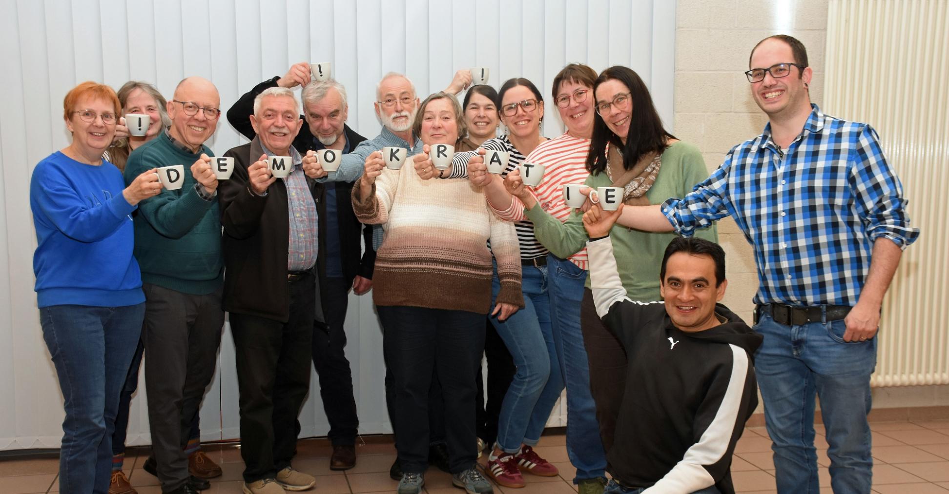 Die Mitglieder des Pfarrgemeinderates halten mit Buchstaben bedruckte Tassen, die zusammen das Wort Demokratie ergeben.