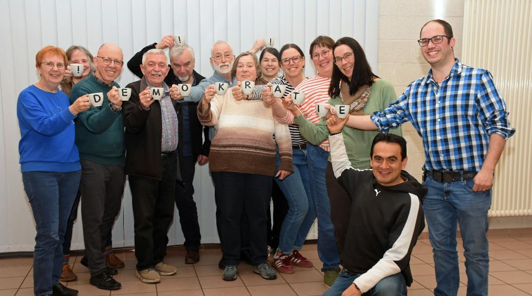 Die Mitglieder des Pfarrgemeinderates halten mit Buchstaben bedruckte Tassen, die zusammen das Wort Demokratie ergeben.