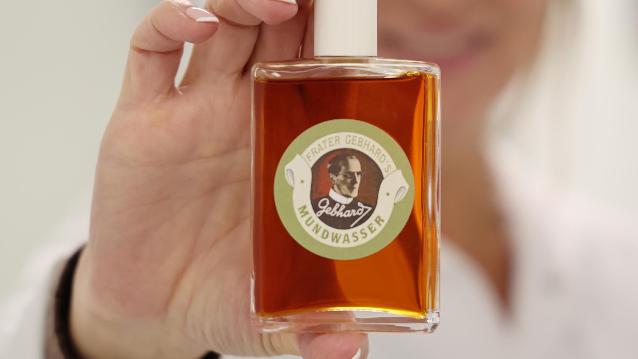 Eine Frau hält eine Flasche mit bräunlicher Flüssigkeit in die Kamera