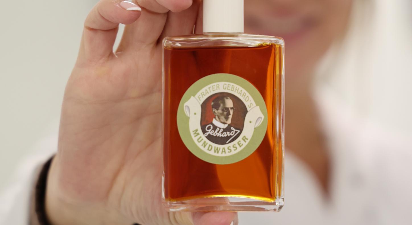 Eine Frau hält eine Flasche mit bräunlicher Flüssigkeit in die Kamera