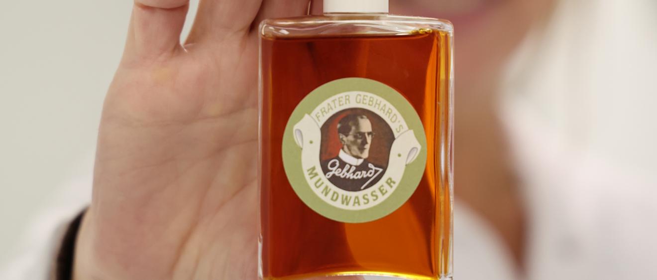 Eine Frau hält eine Flasche mit bräunlicher Flüssigkeit in die Kamera