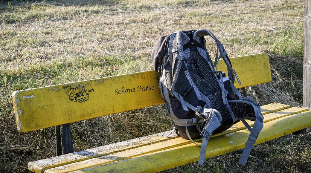 Ein Rucksack steht auf einer gelben Bank vor einer Wiese