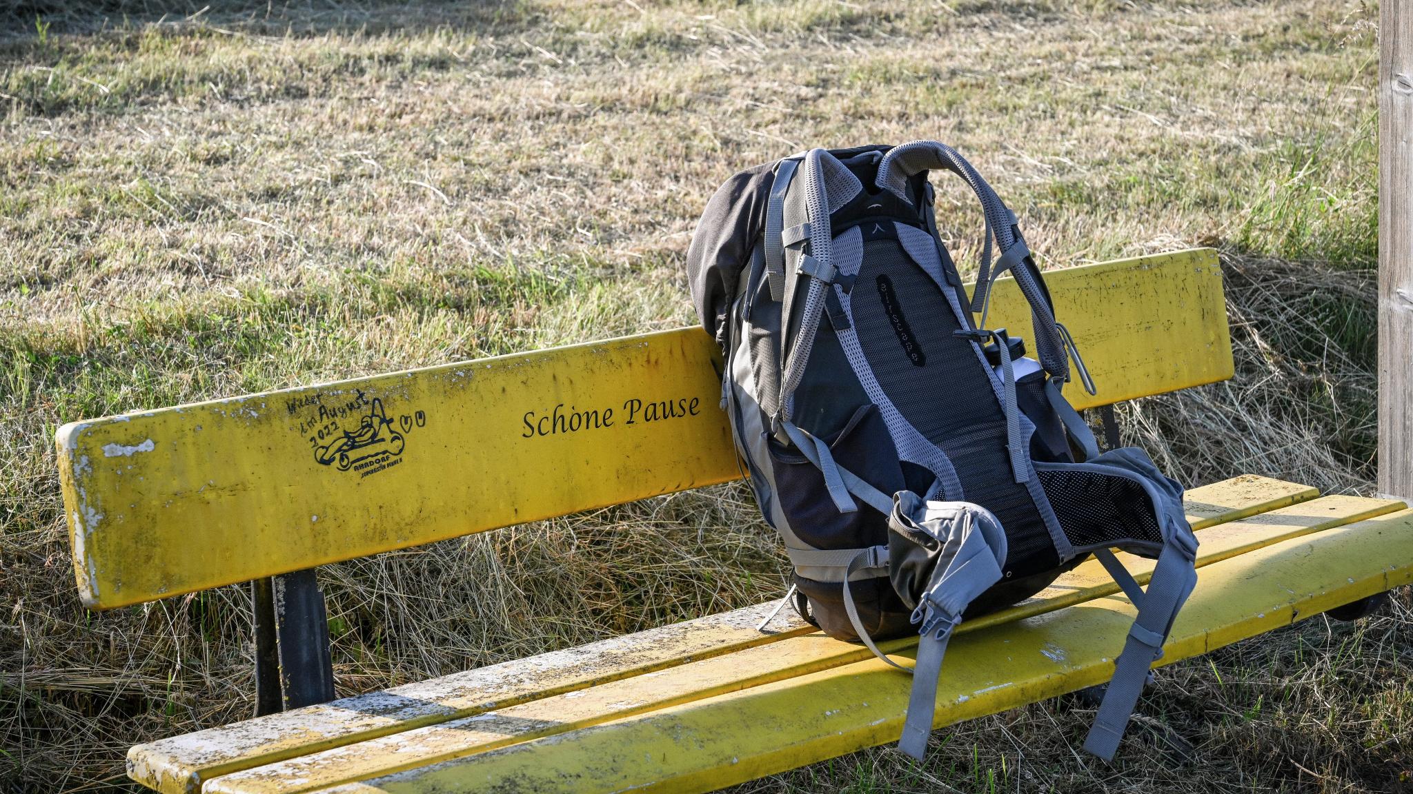 Ein Rucksack steht auf einer gelben Bank vor einer Wiese