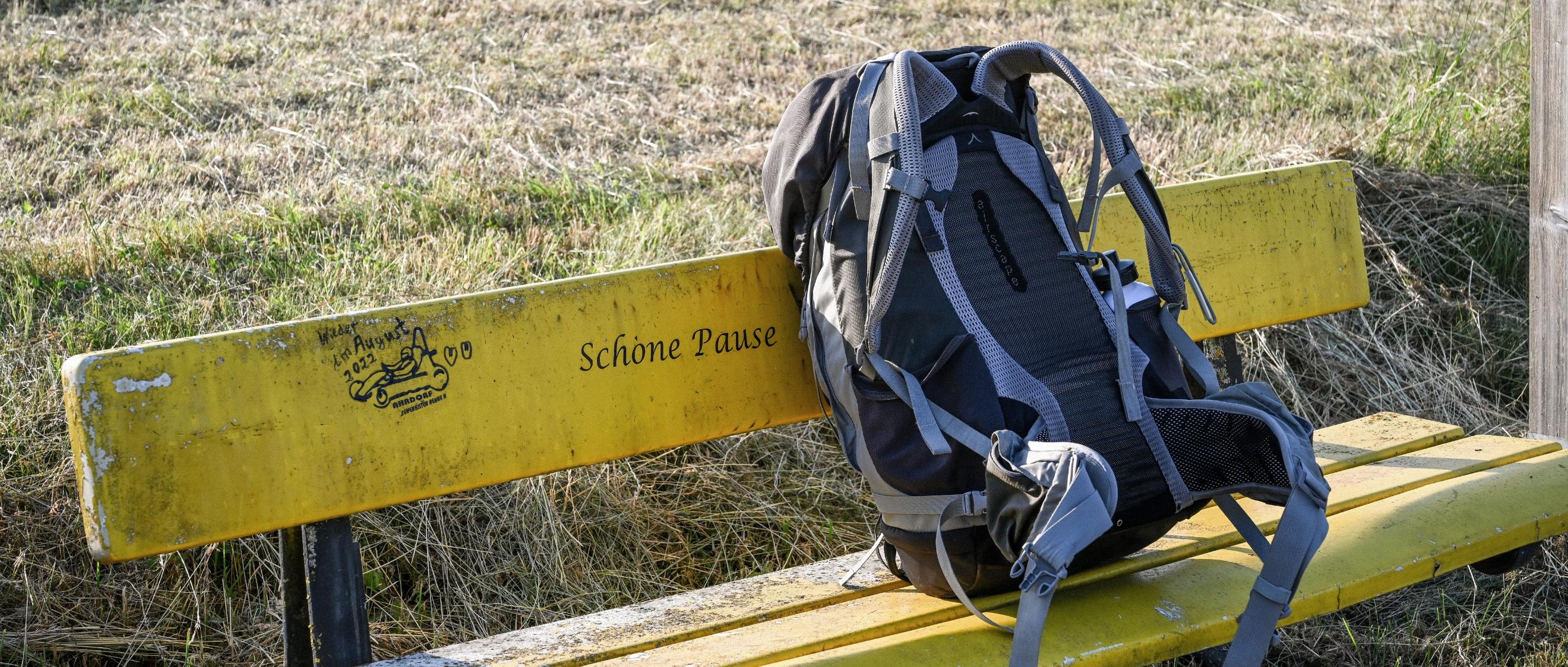 Ein Rucksack steht auf einer gelben Bank vor einer Wiese