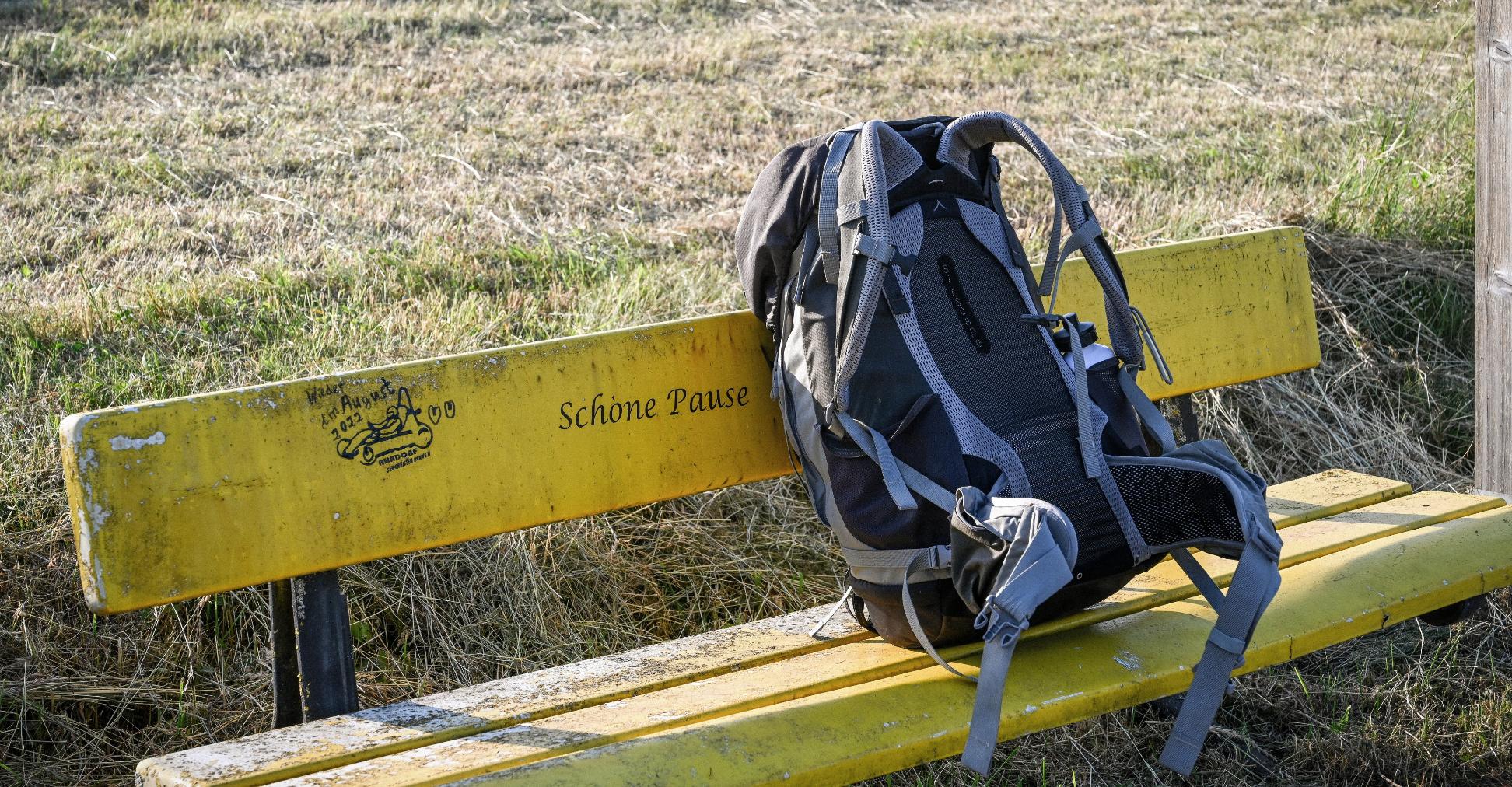 Ein Rucksack steht auf einer gelben Bank vor einer Wiese