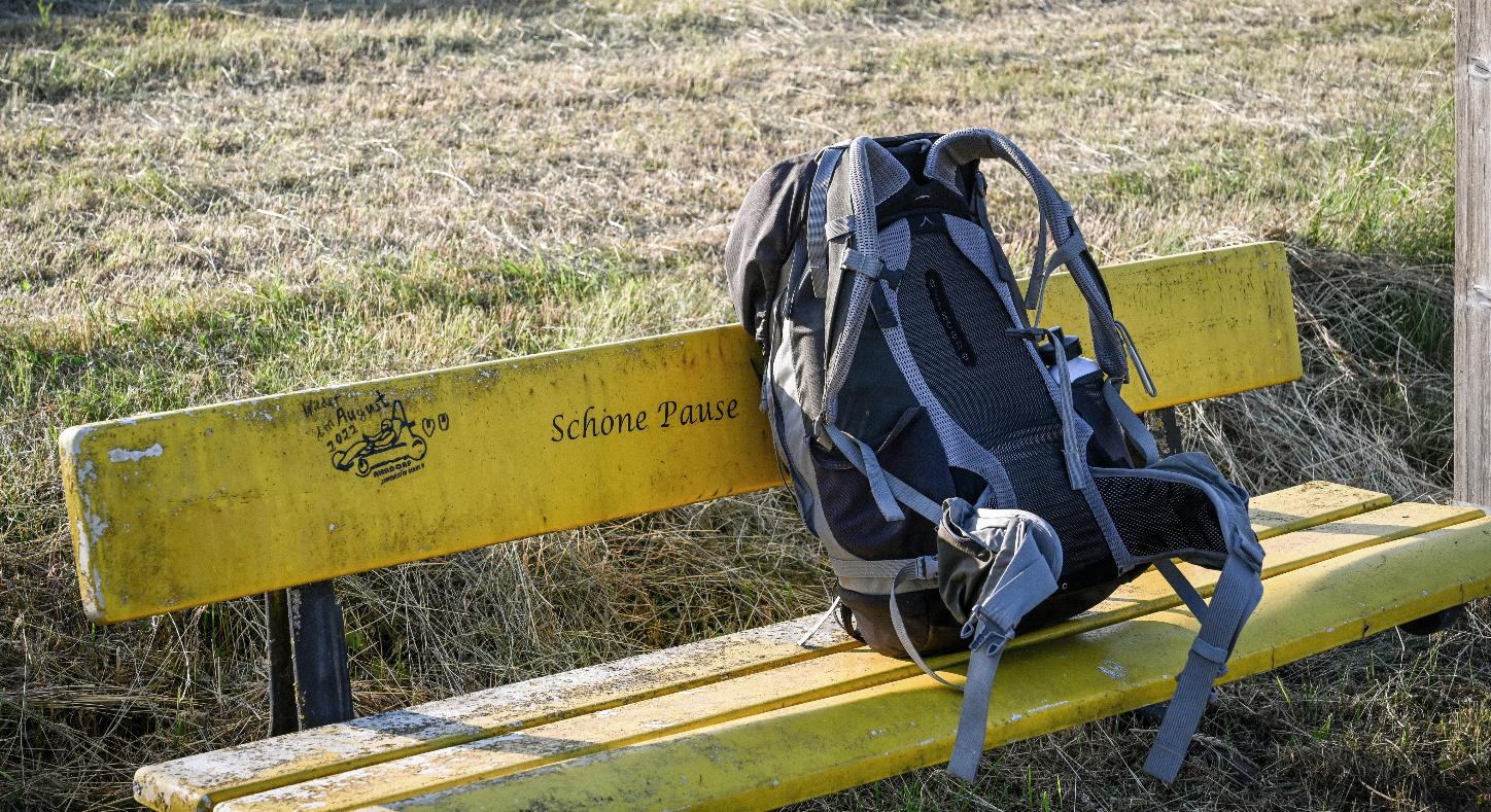Ein Rucksack steht auf einer gelben Bank vor einer Wiese