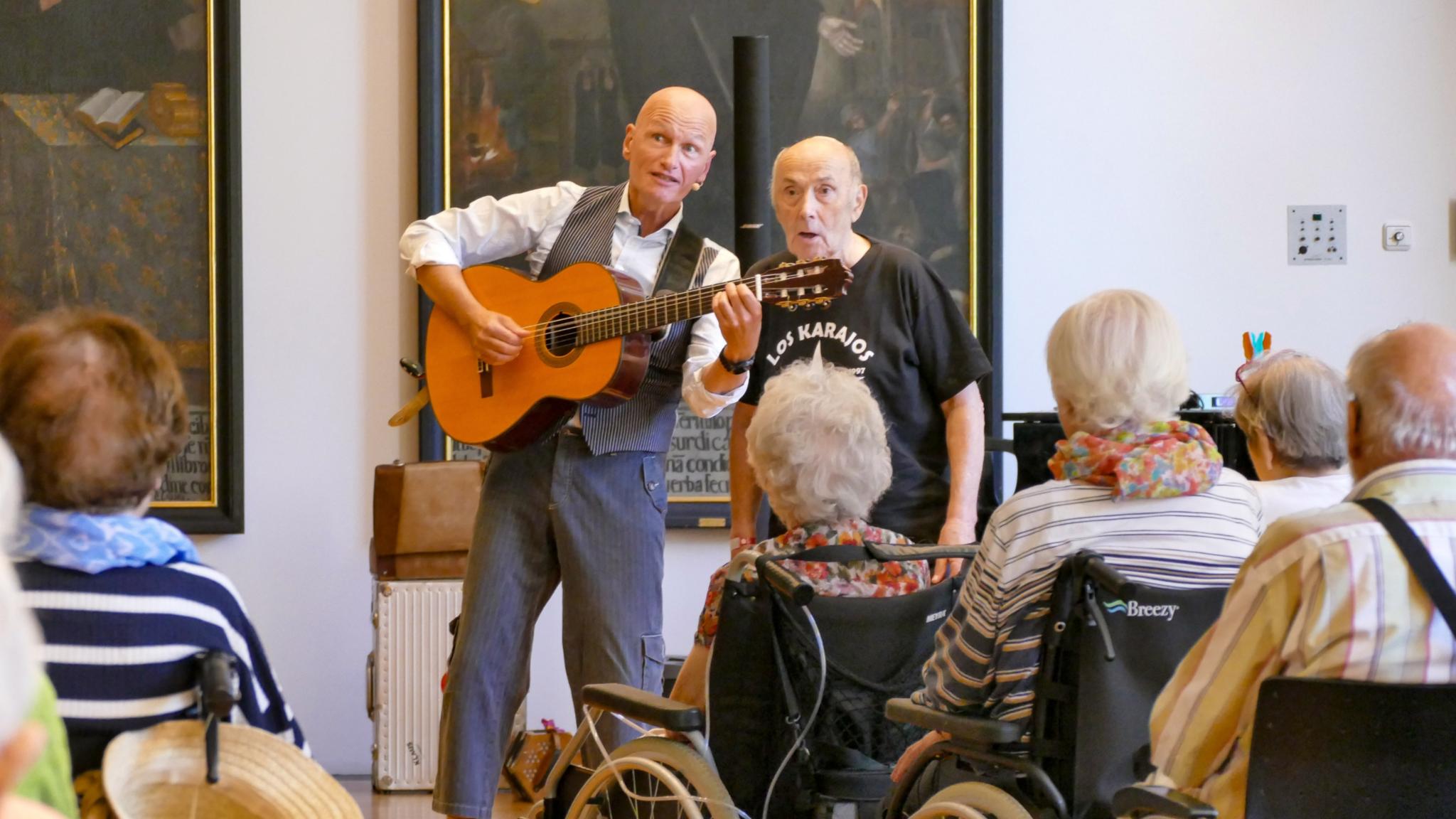 Ein Mann mit Gitarre singt mit einem anderen Mann vor Publikum