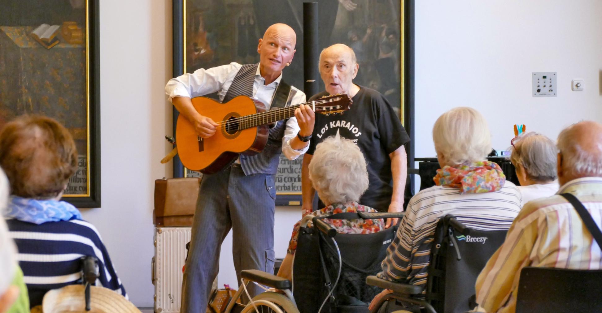 Ein Mann mit Gitarre singt mit einem anderen Mann vor Publikum
