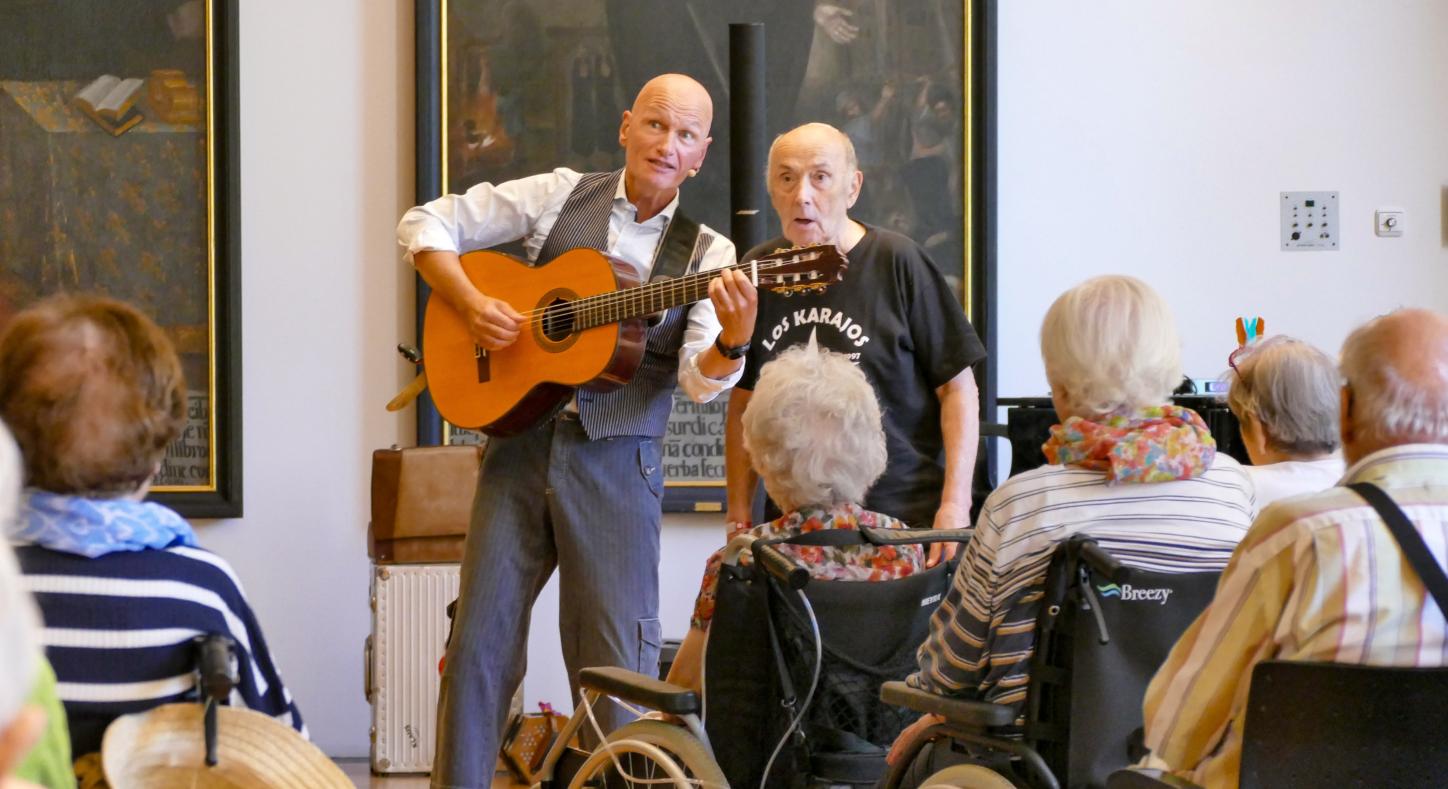 Ein Mann mit Gitarre singt mit einem anderen Mann vor Publikum