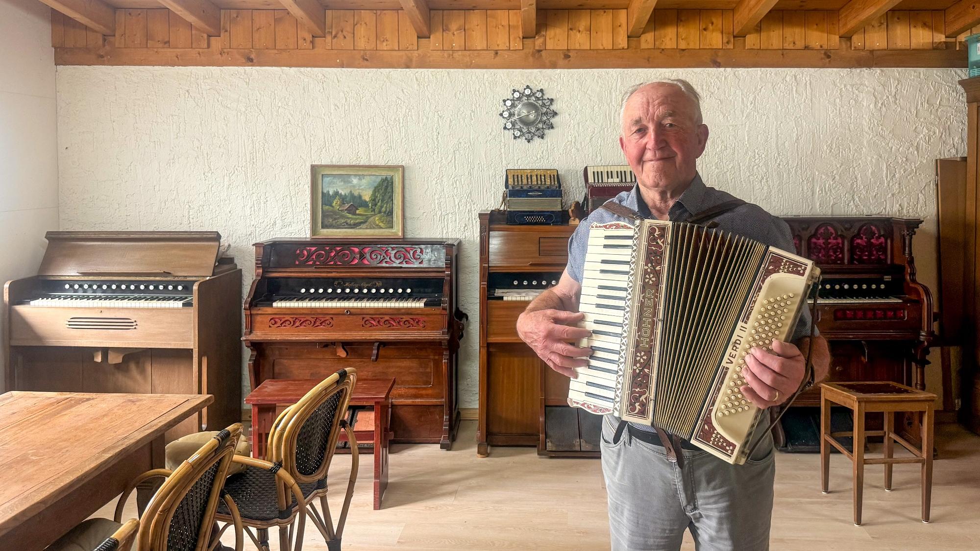 Ein Mann mit einem Harmonium steht vor verschiedenen alten Orgeln