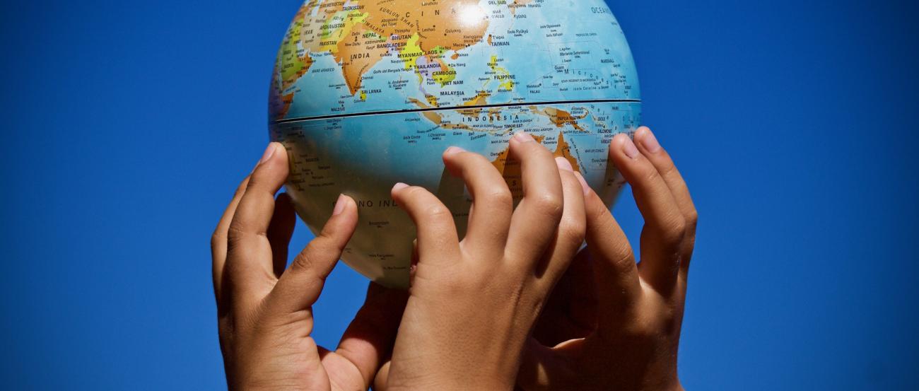 vier Hände halten eine handballgroße Erde mit den Fingerspitzen