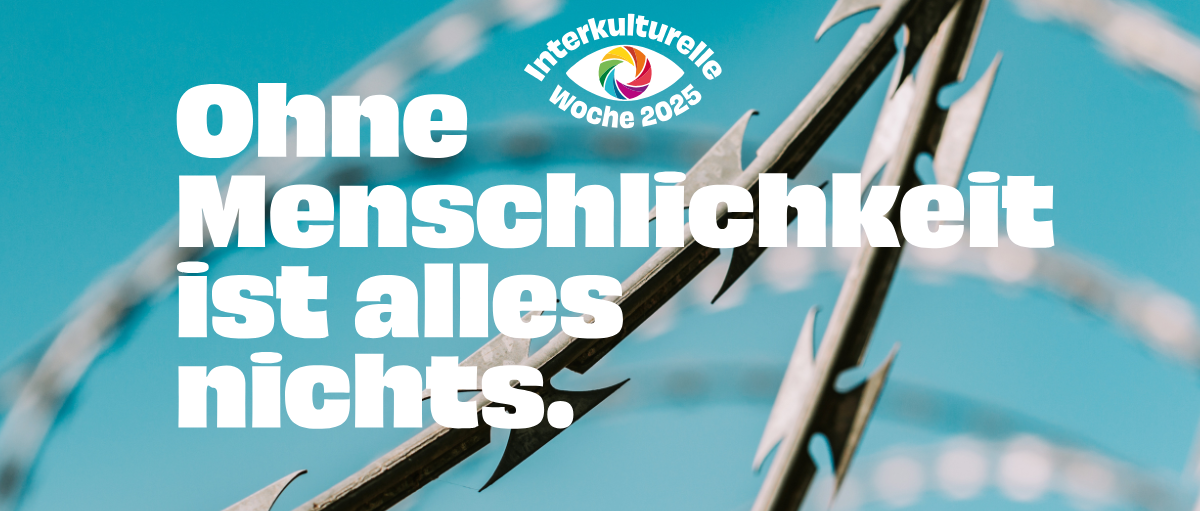 Im Hintergrund ist ein Stacheldrahtzaun zu sehen, im Vordergrund steht: 'Ohne Menschlichkeit ist alles nichts.'